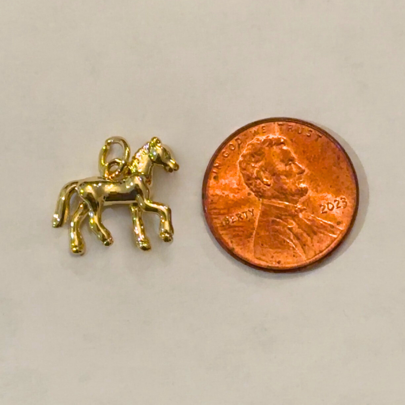 Gold horse charm next to a penny on a light gray background