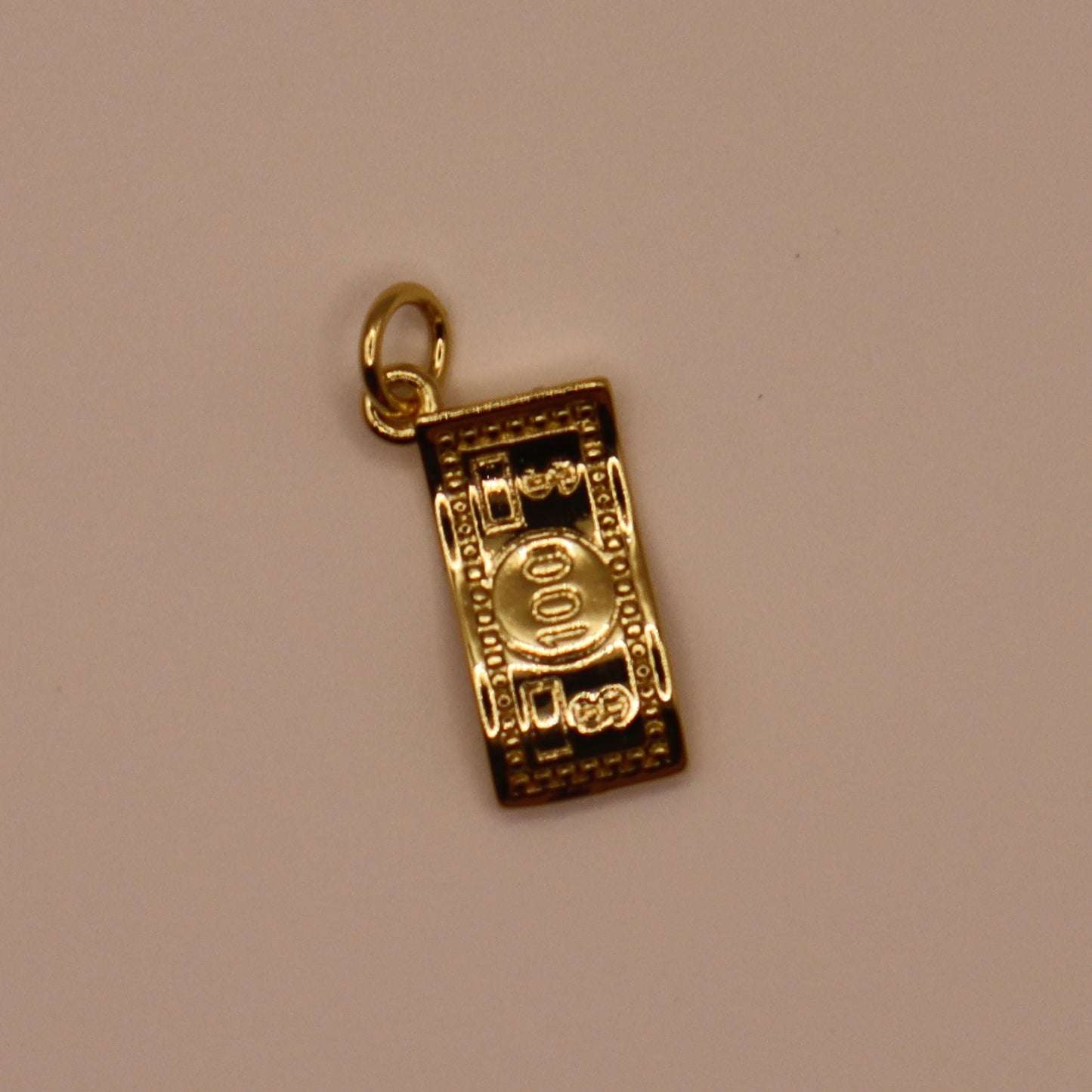 Gold charm resembling a roll of money on a beige background