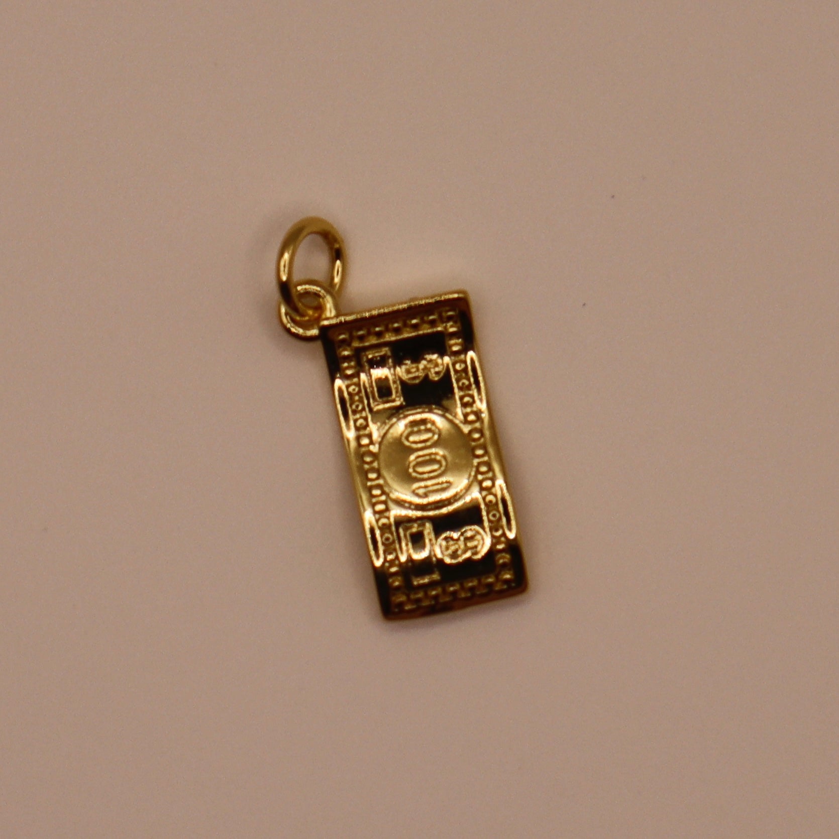 Gold charm resembling a roll of money on a beige background