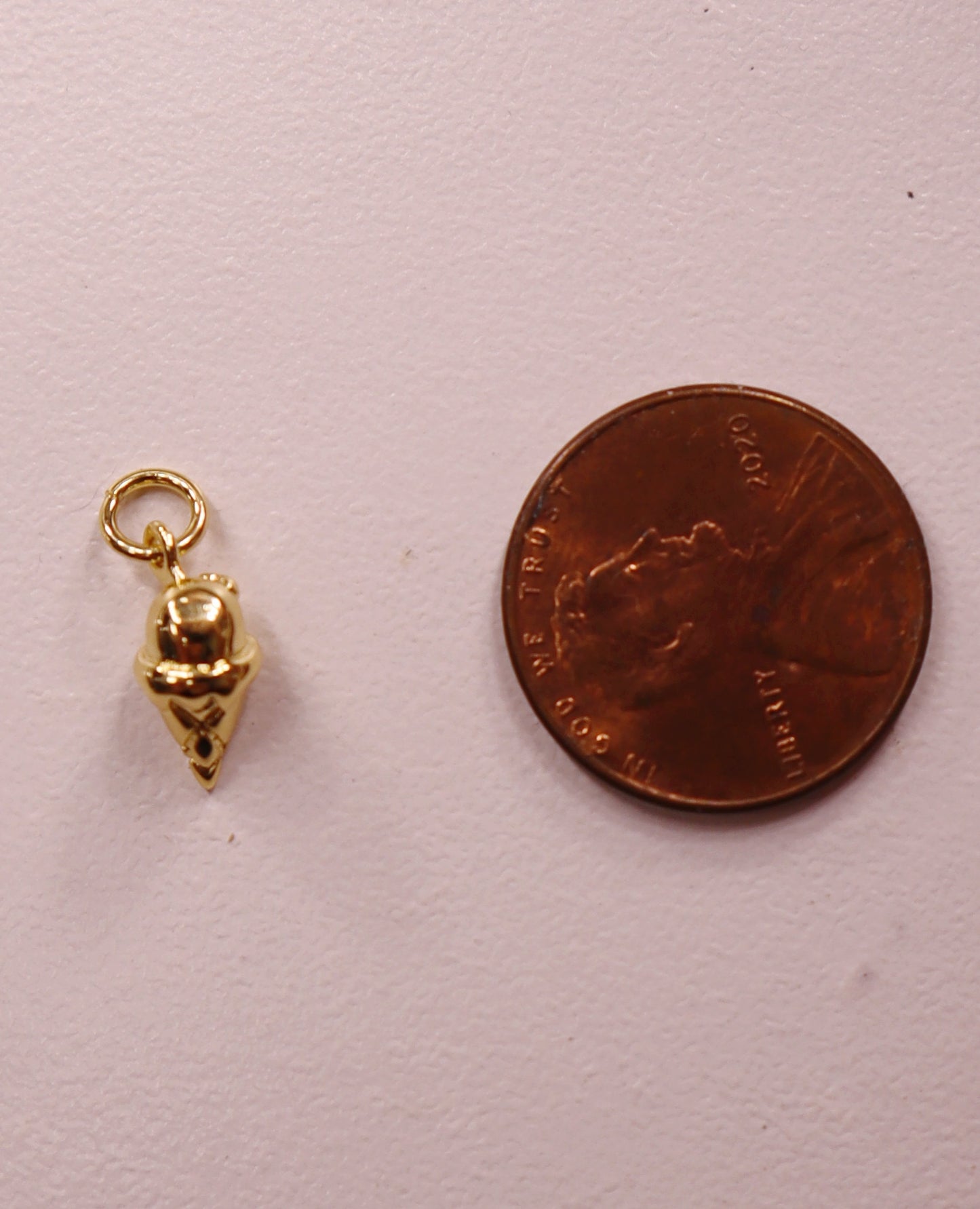 Gold ice cream charm next to a penny on a light pink background