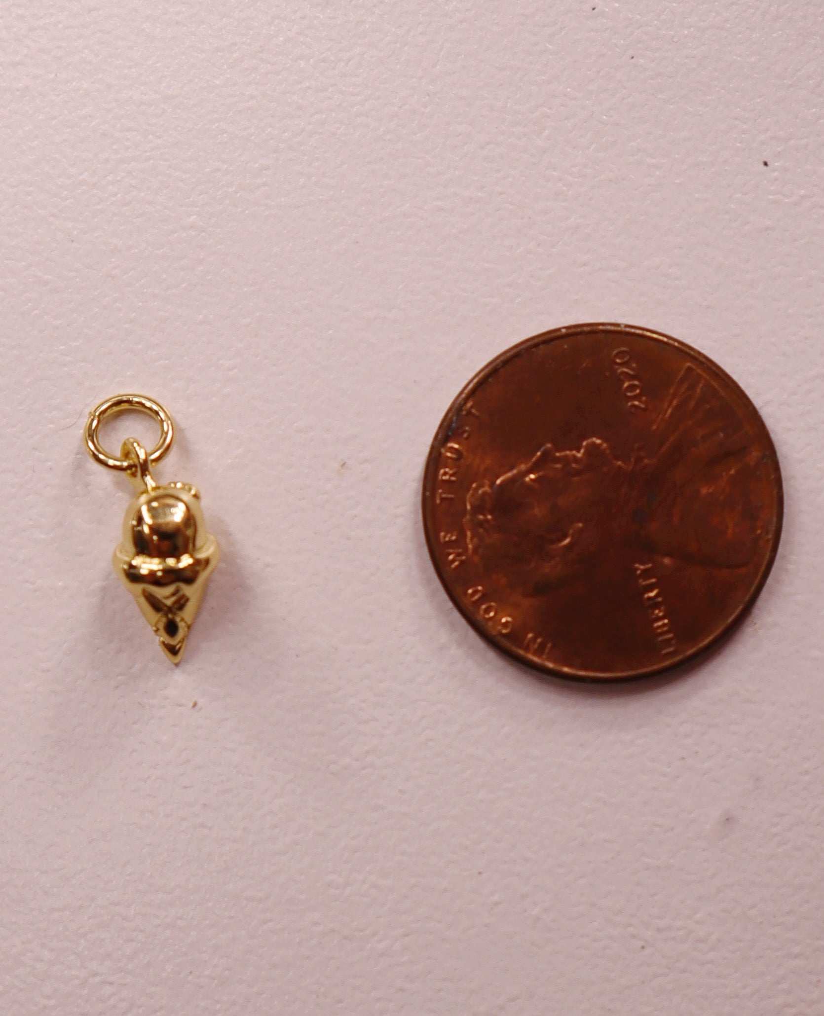 Gold ice cream charm next to a penny on a light pink background