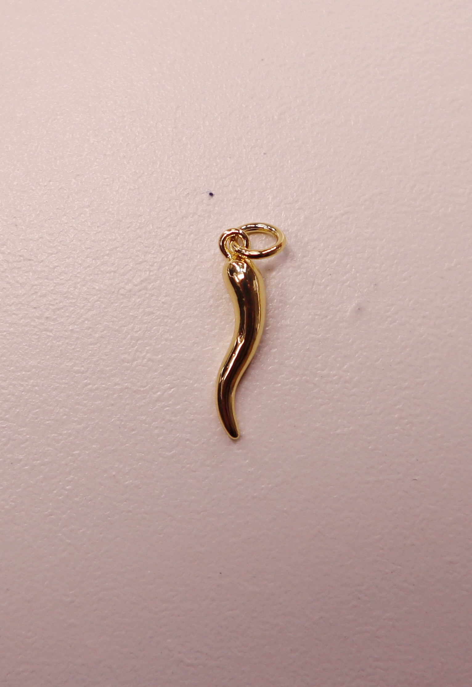 Gold Italian horn-shaped pendant on a light pink background