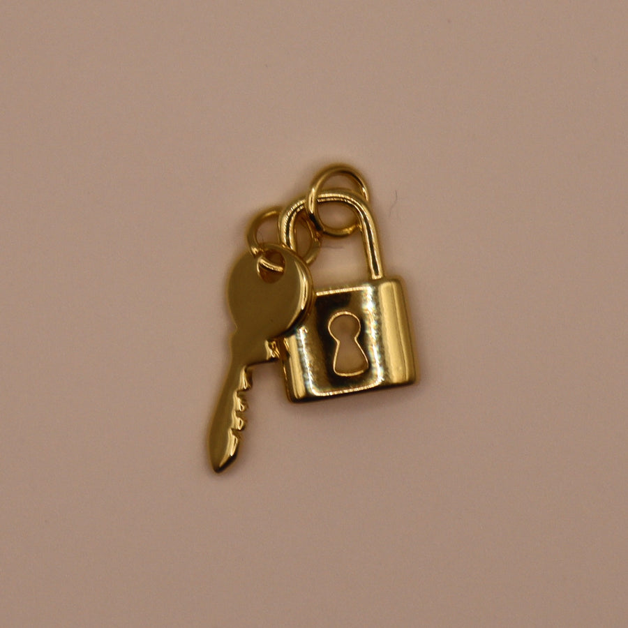 Gold key and lock charm on a beige background