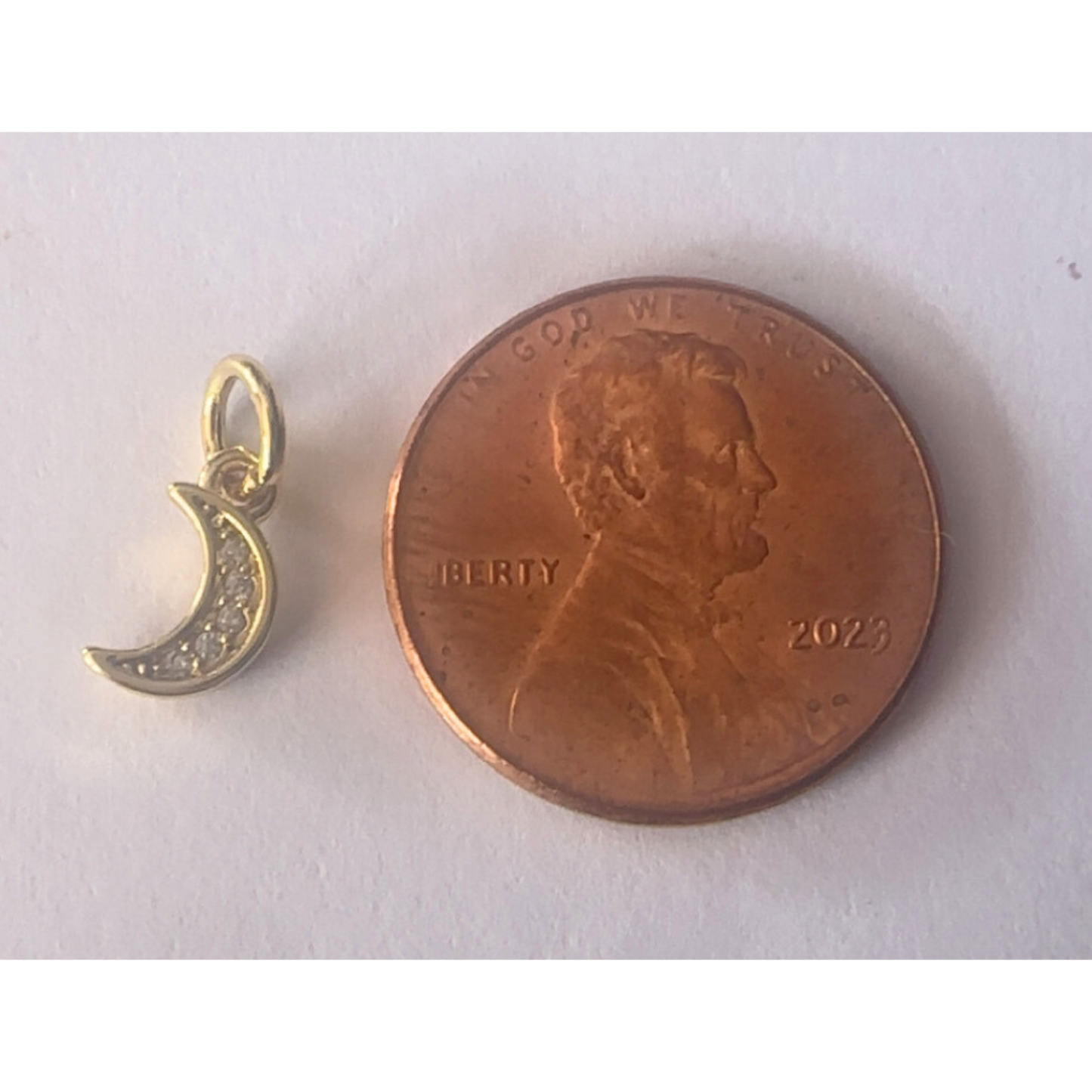 Gold crescent moon pendant next to a penny on a white background