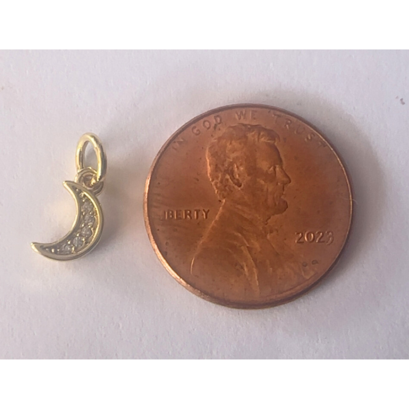 Gold crescent moon pendant next to a penny on a white background