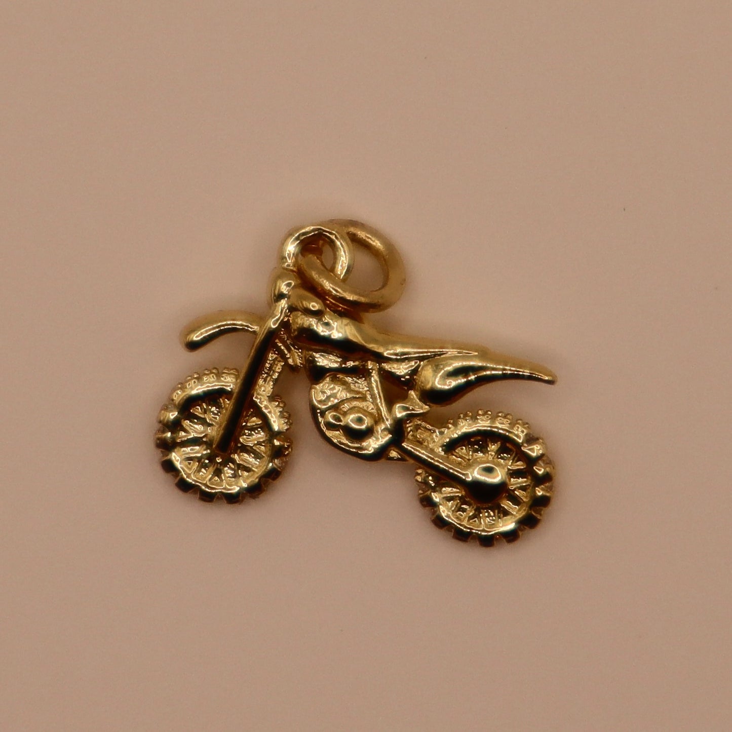 Gold motorcycle charm on a beige background