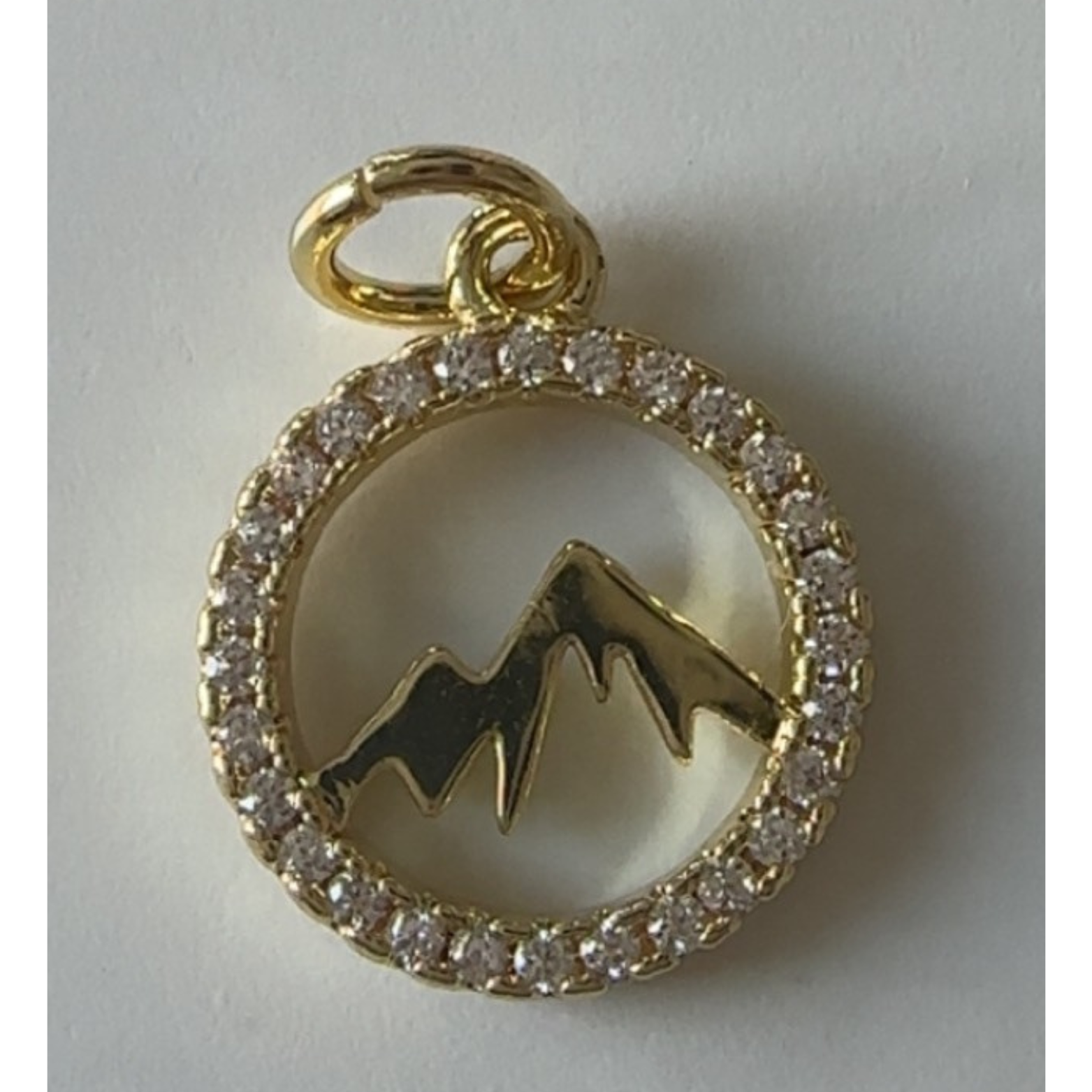 Gold pendant with mountain design and diamond-like stones on a white background