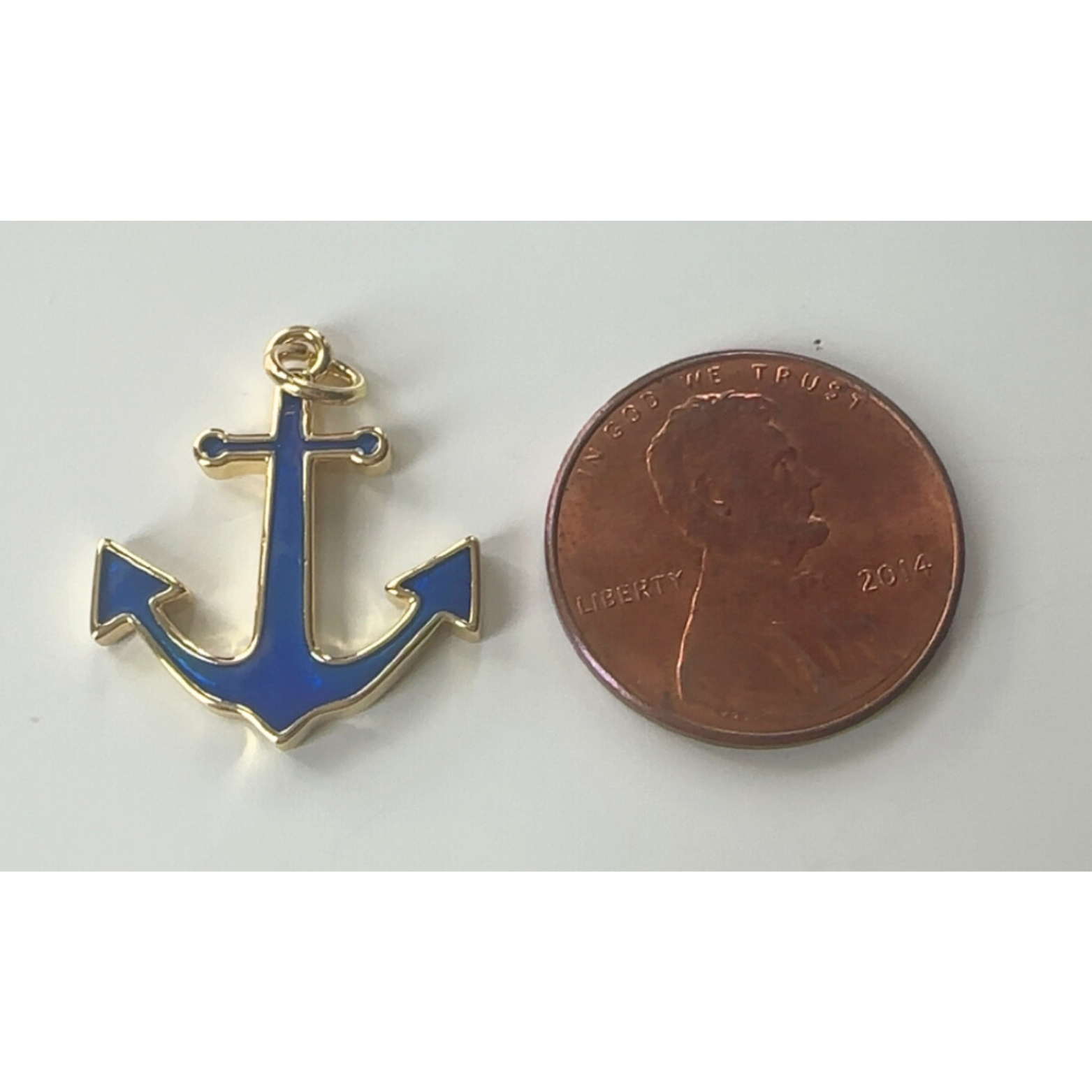Blue anchor pendant next to a penny on a white background