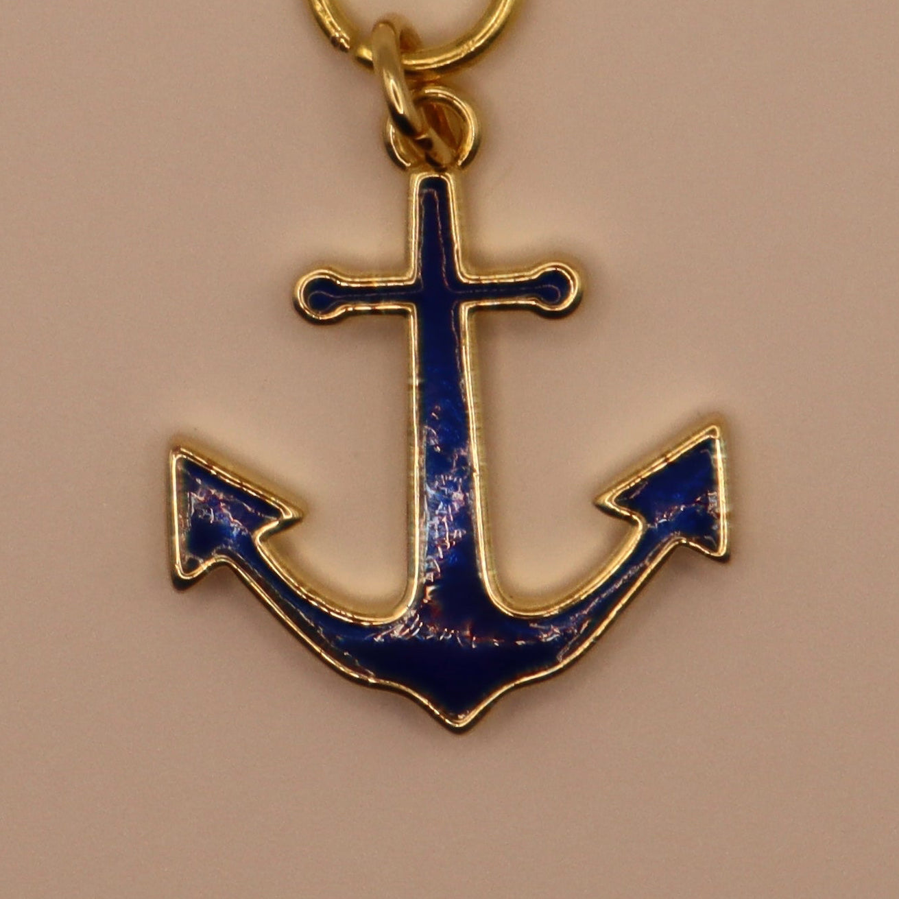 Gold anchor pendant with blue enamel on a beige background