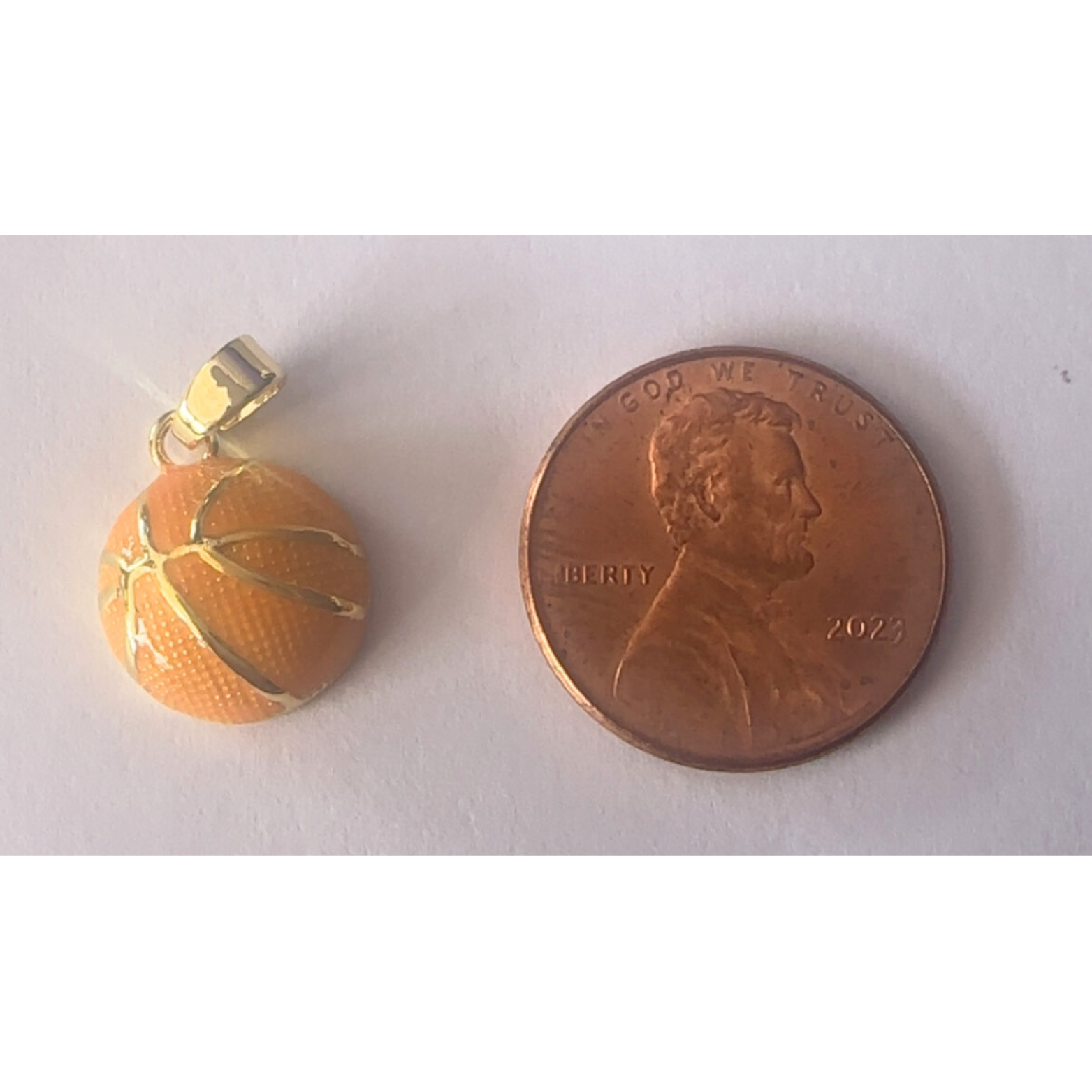 Small basketball charm next to a penny on a white background