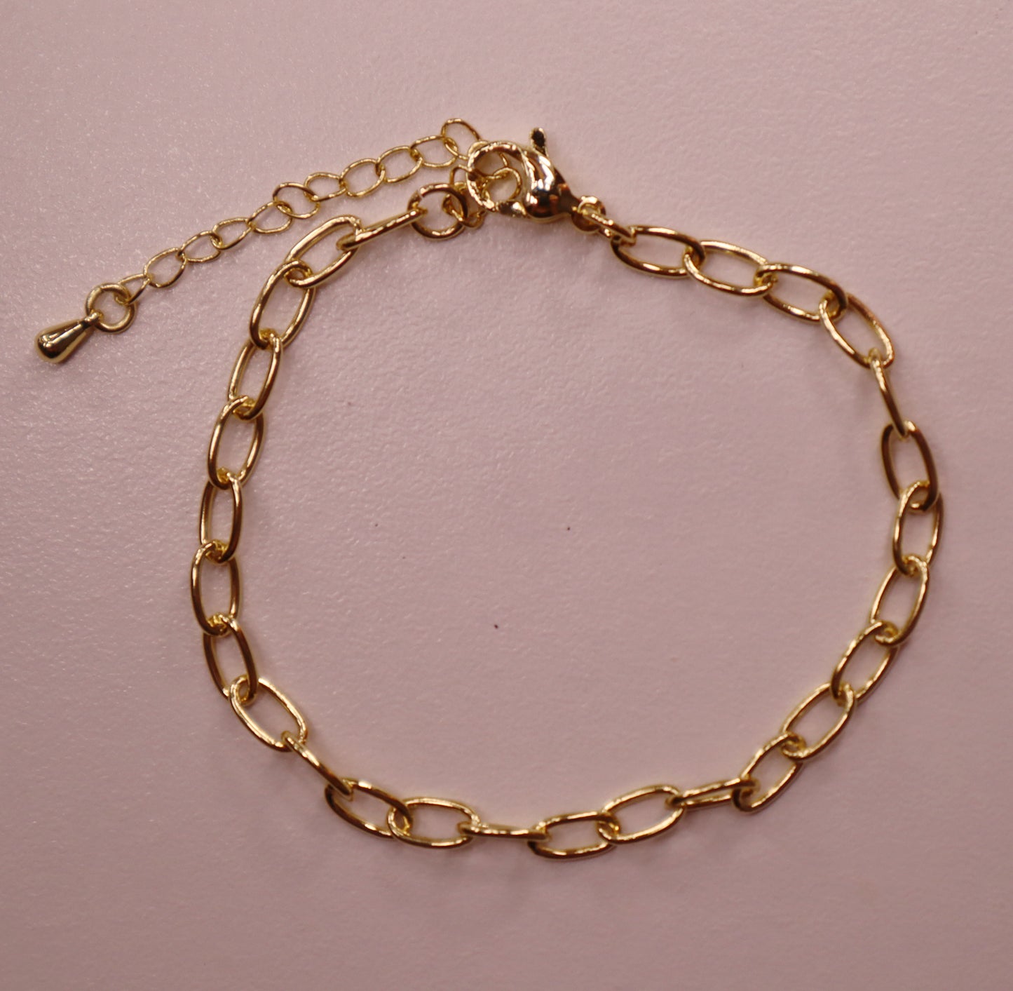 Gold oval chain bracelet on a pink background