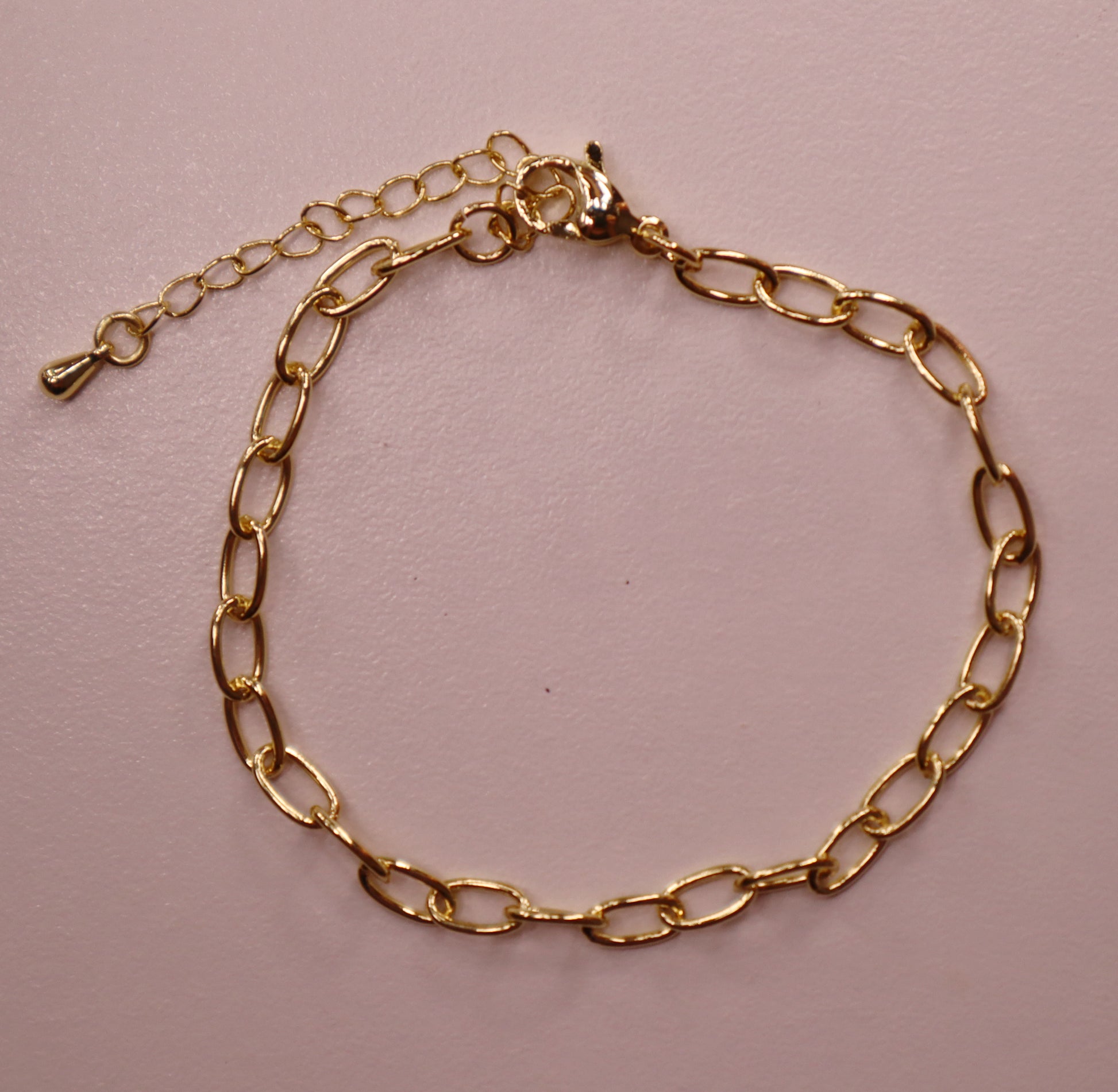 Gold oval chain bracelet on a pink background