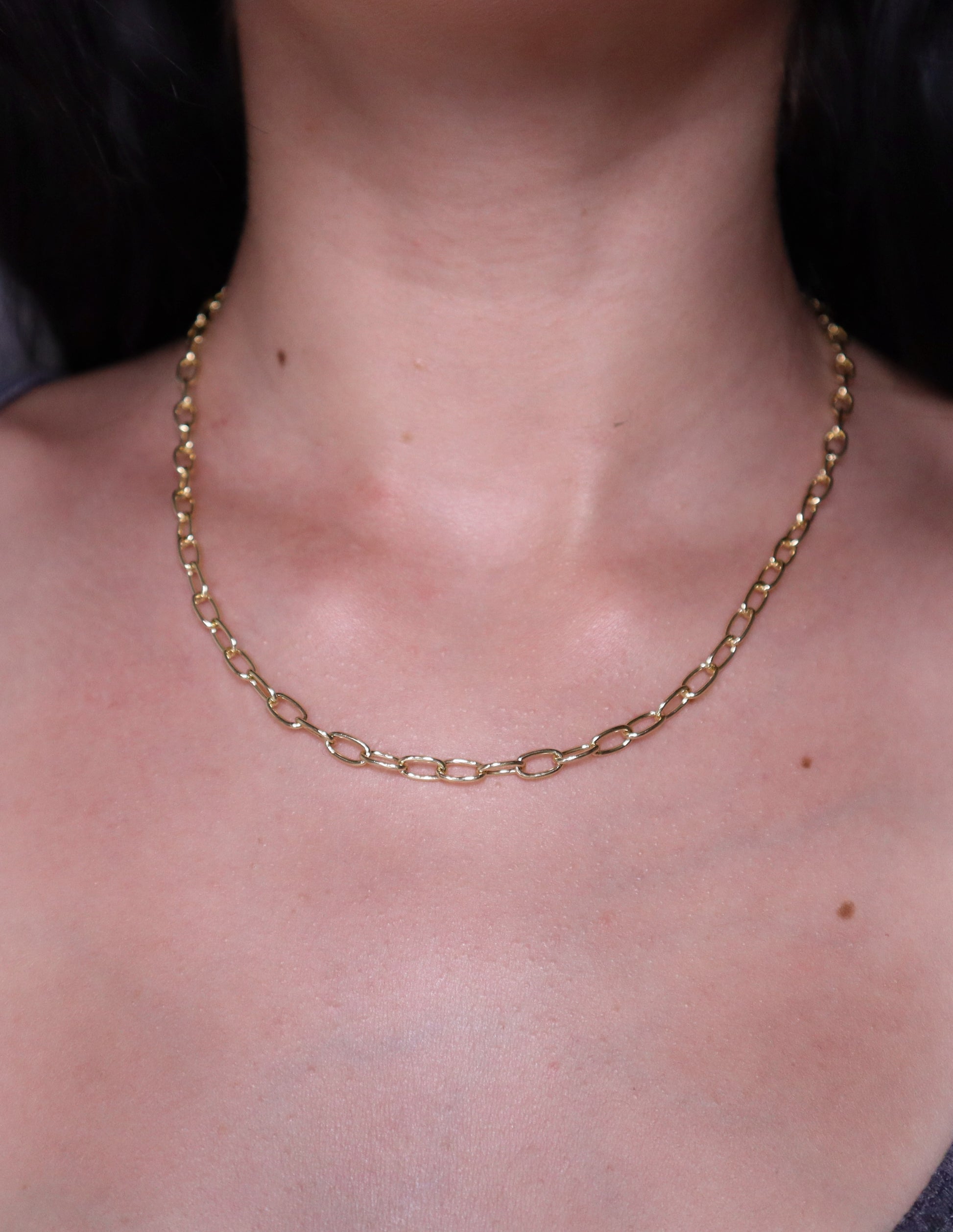Gold oval necklace on a person's neck with a dark background