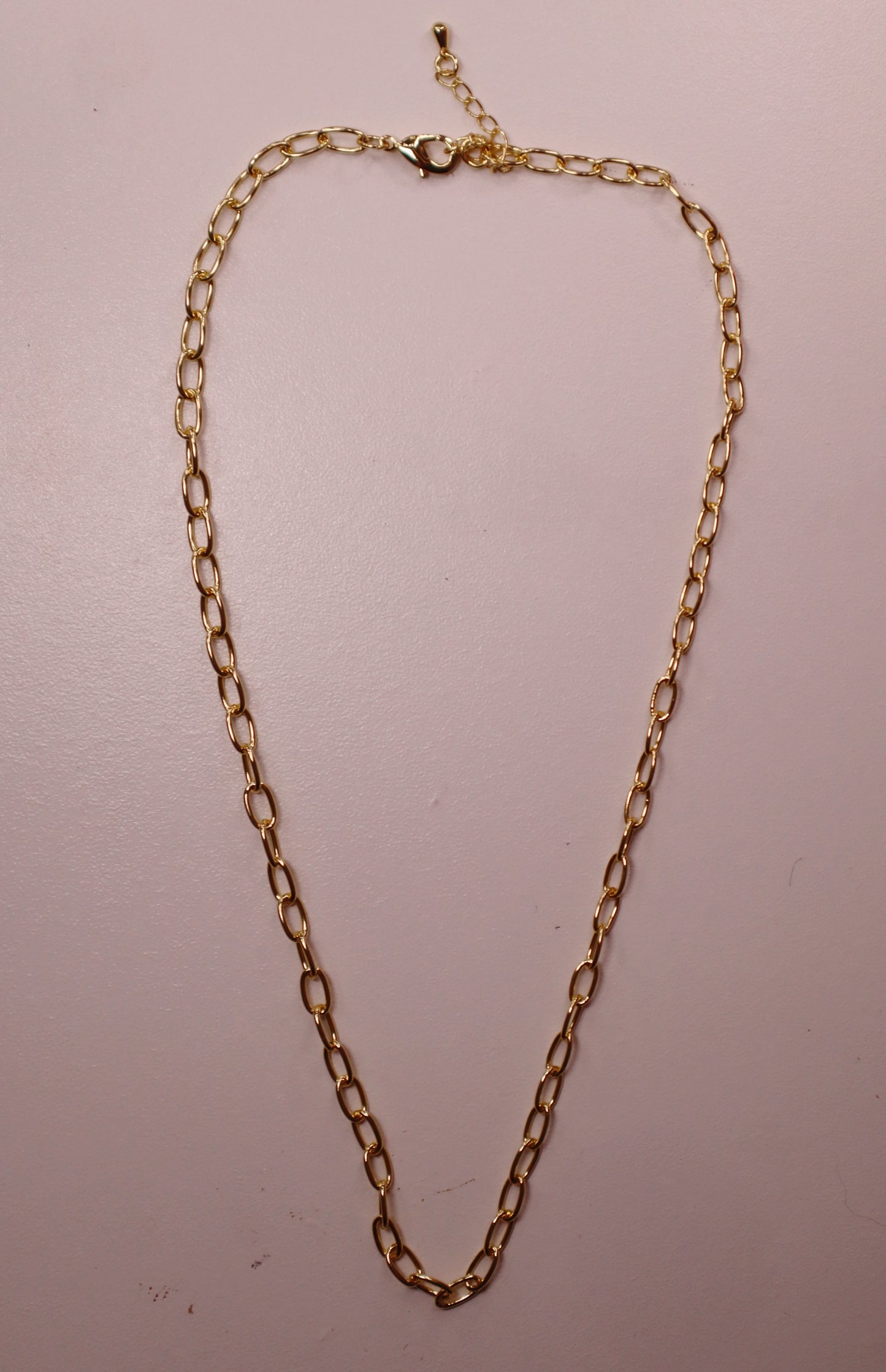 Gold oval necklace on a light pink background