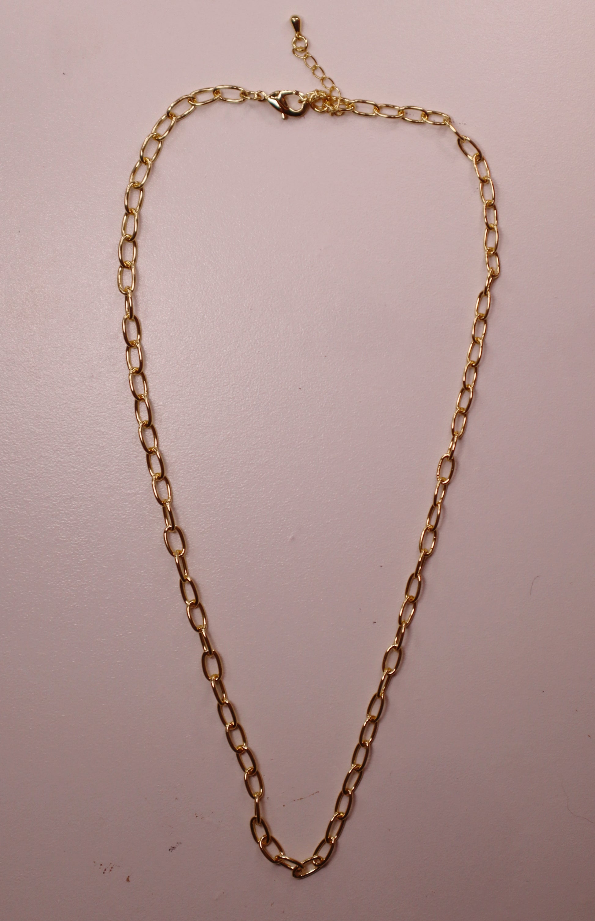 Gold oval necklace on a light pink background