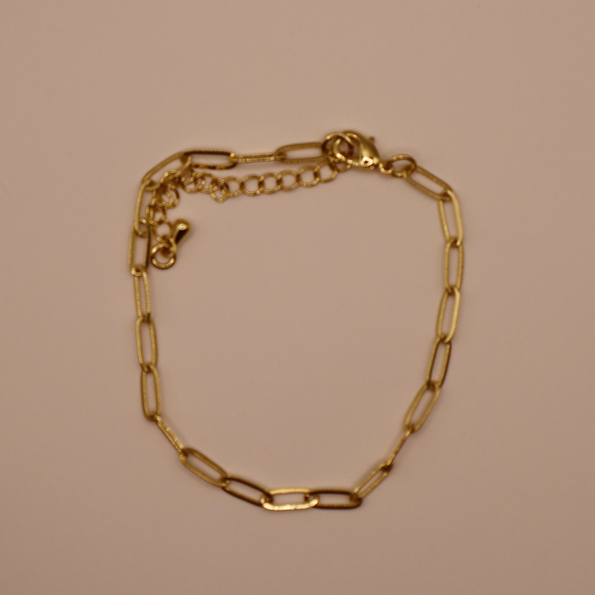 Gold paperclip bracelet on a beige background