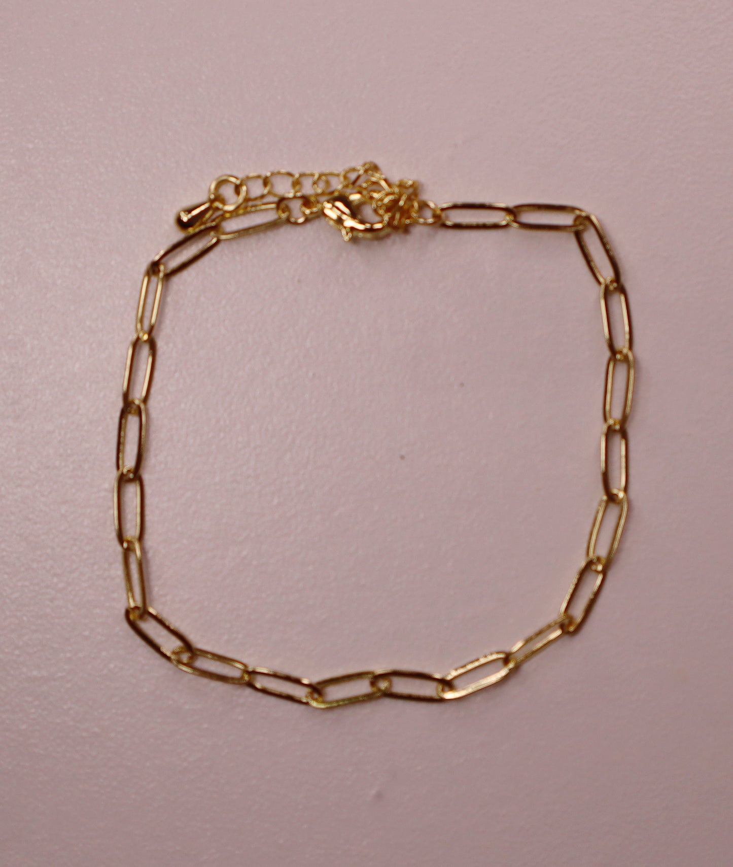 Gold paperclip chain bracelet on a light pink background