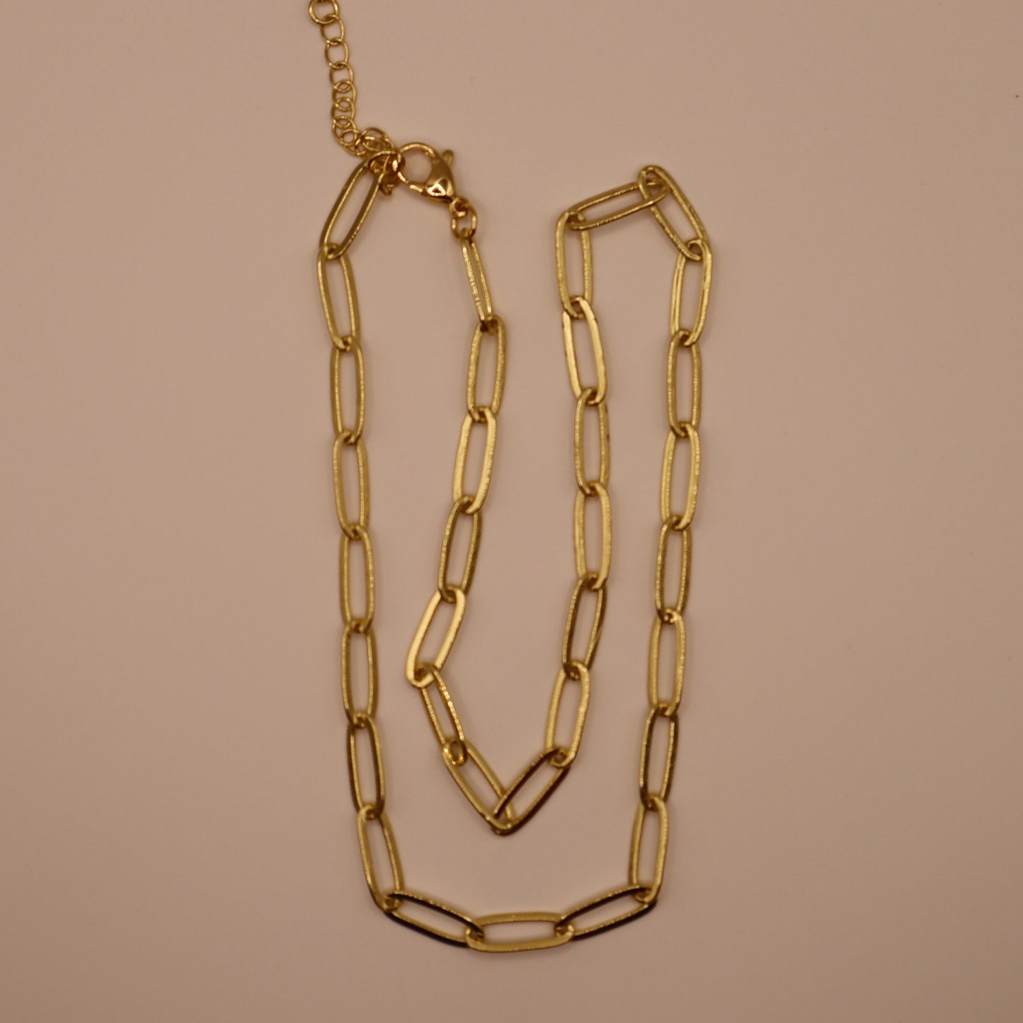 Gold paperclip necklace on a beige background