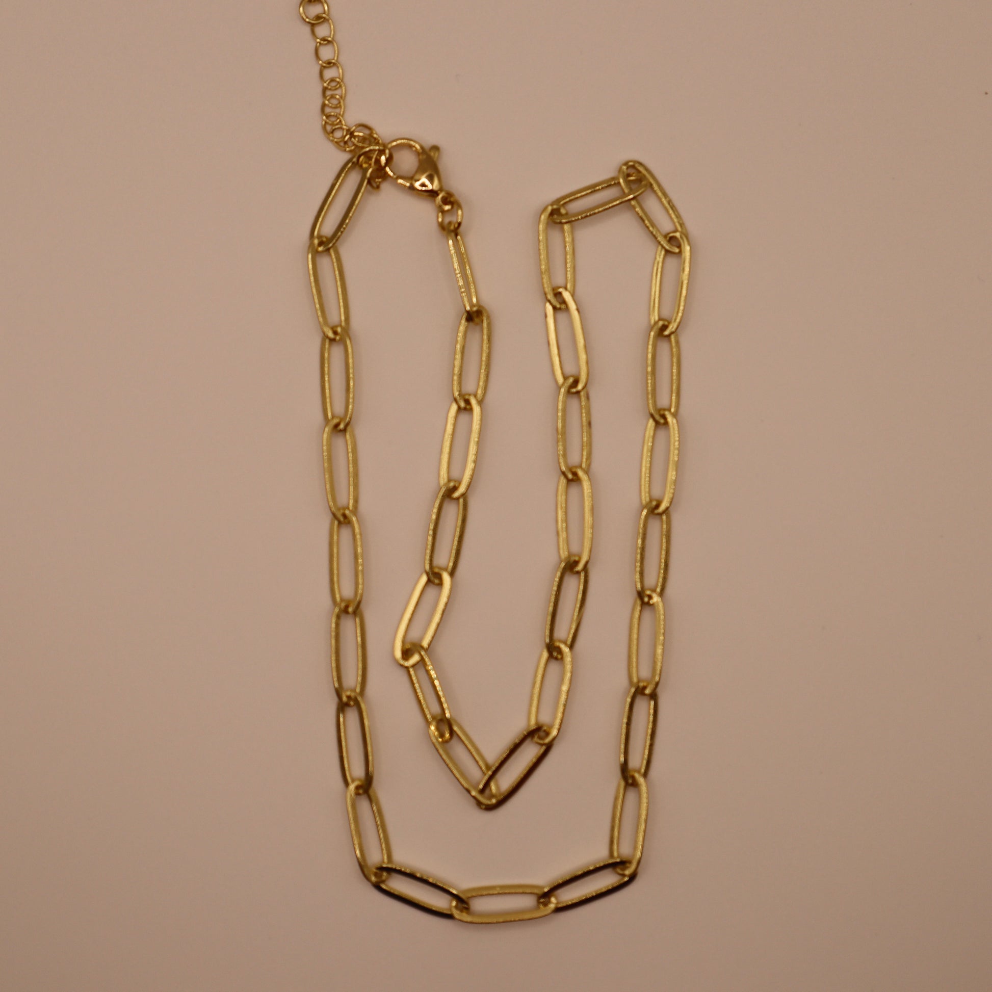 Gold paperclip necklace on a beige background