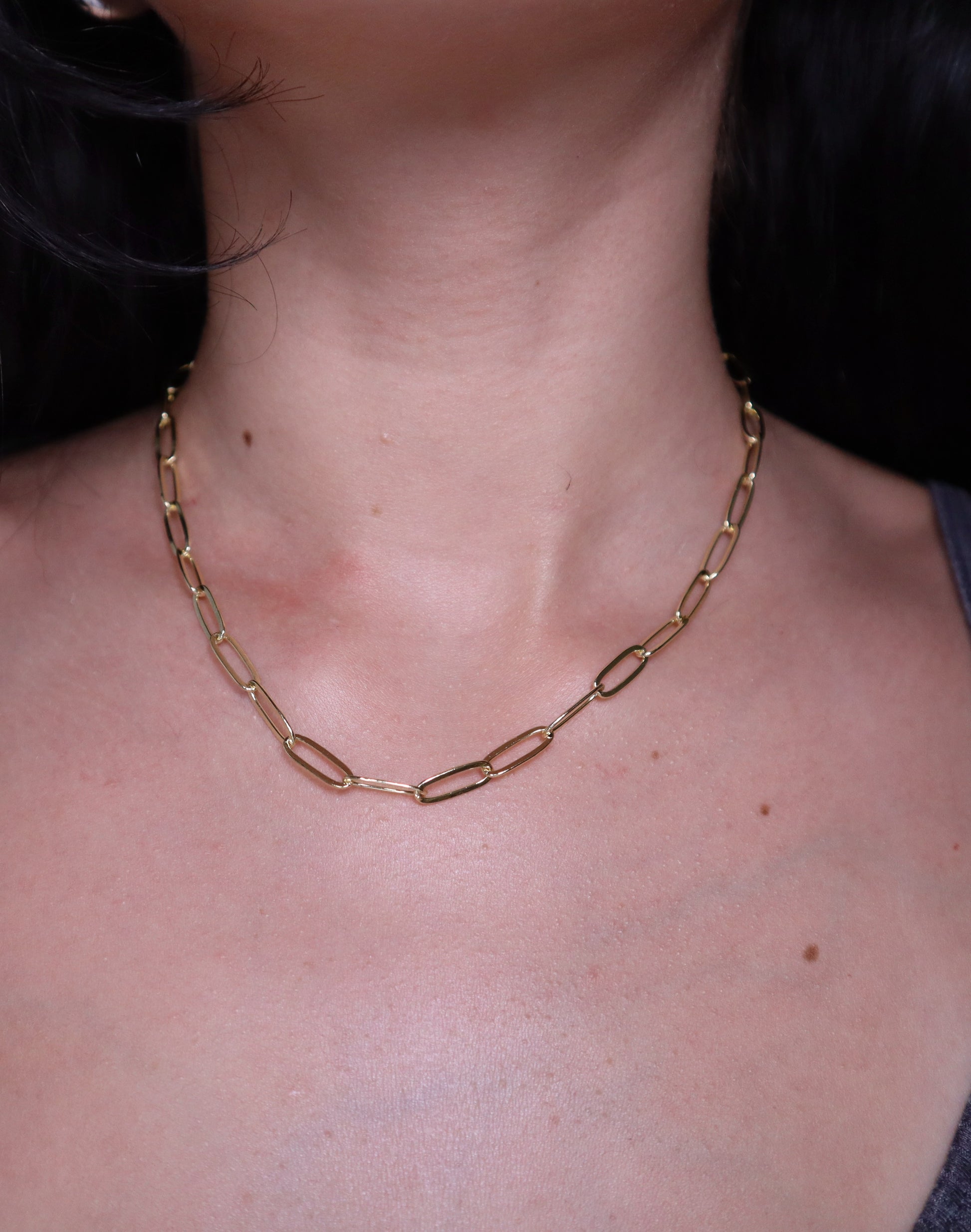 Gold paperclip chain necklace worn by a person with a dark background