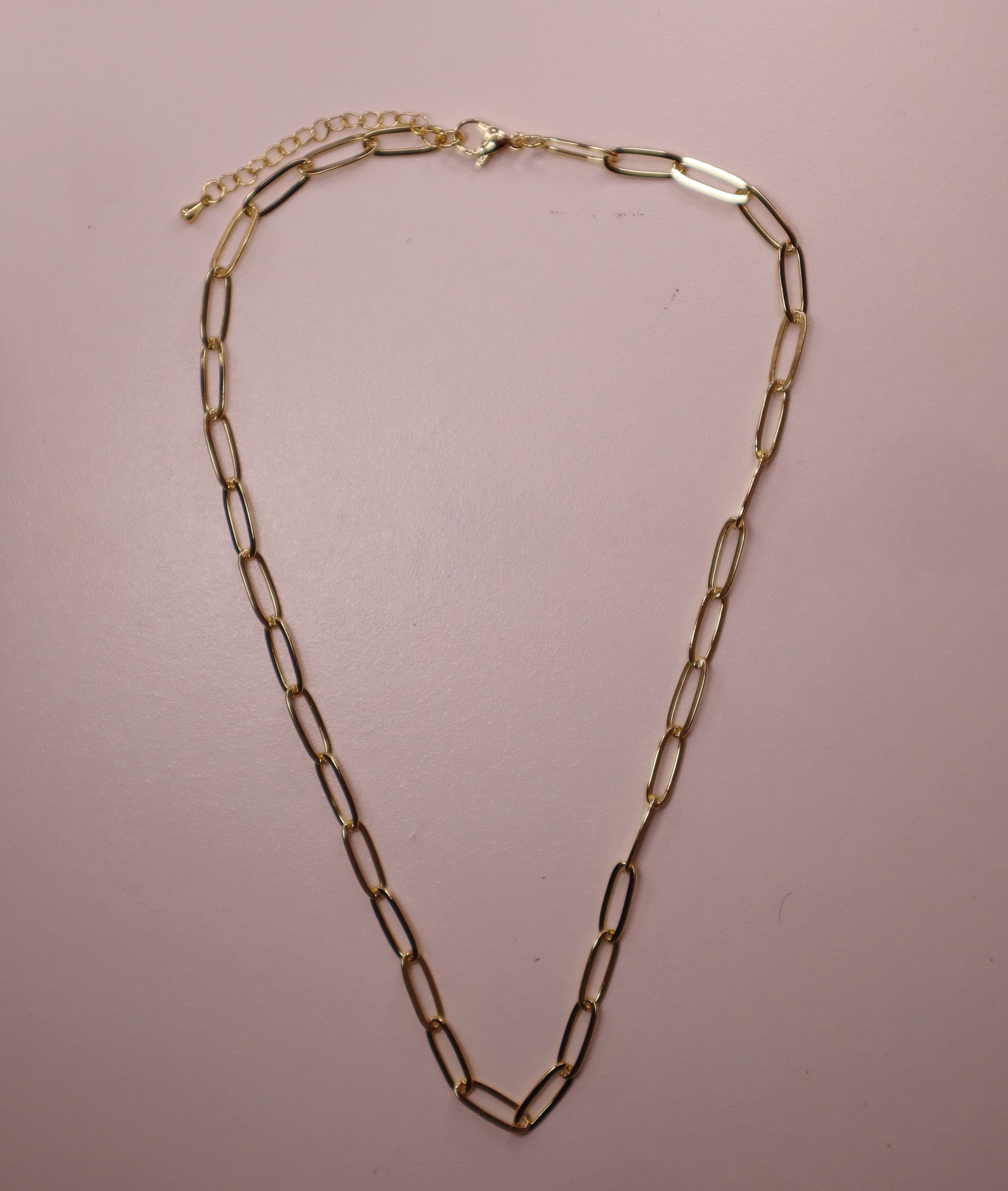 Gold paperclip chain necklace on a pink background