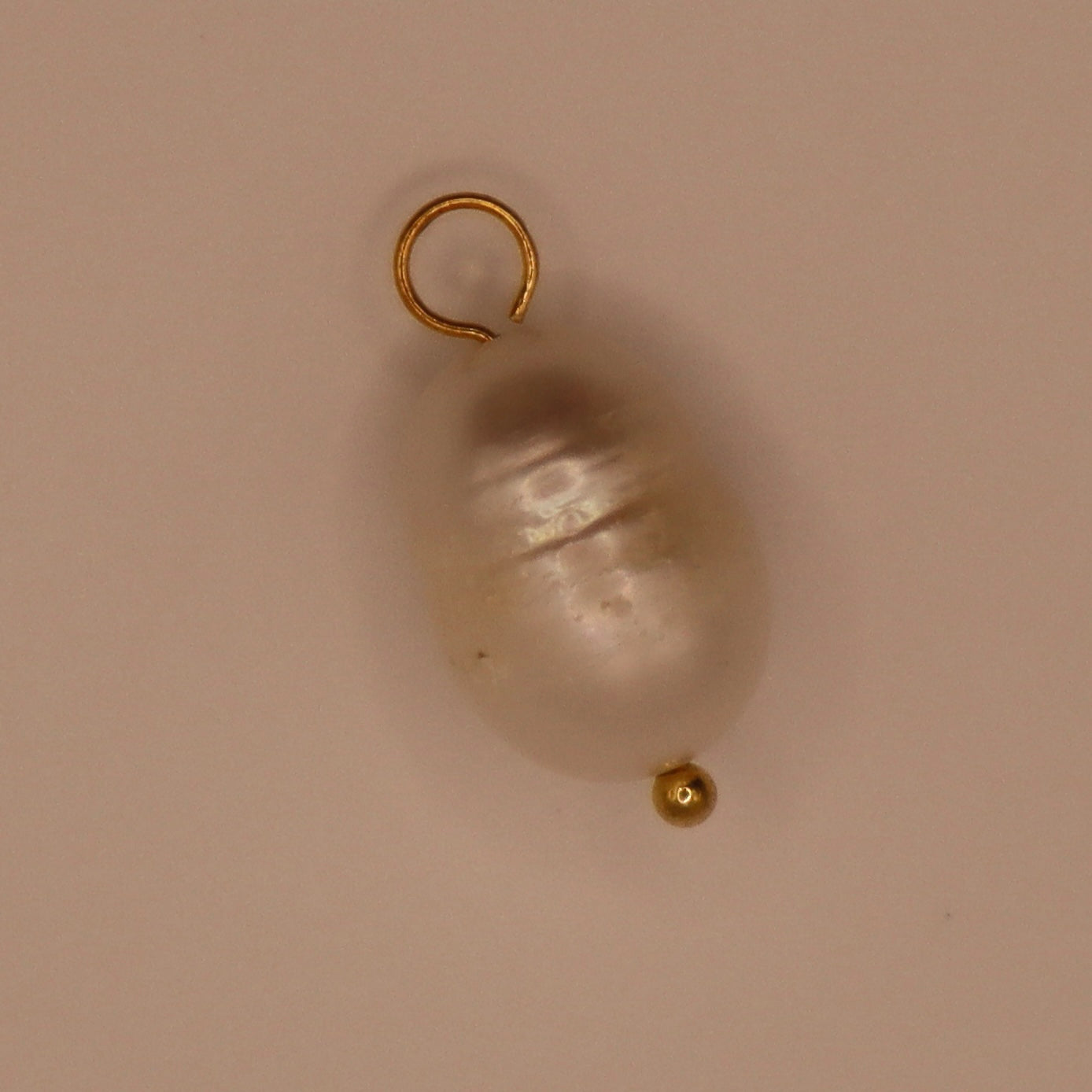 Gold pearl charm on a beige background