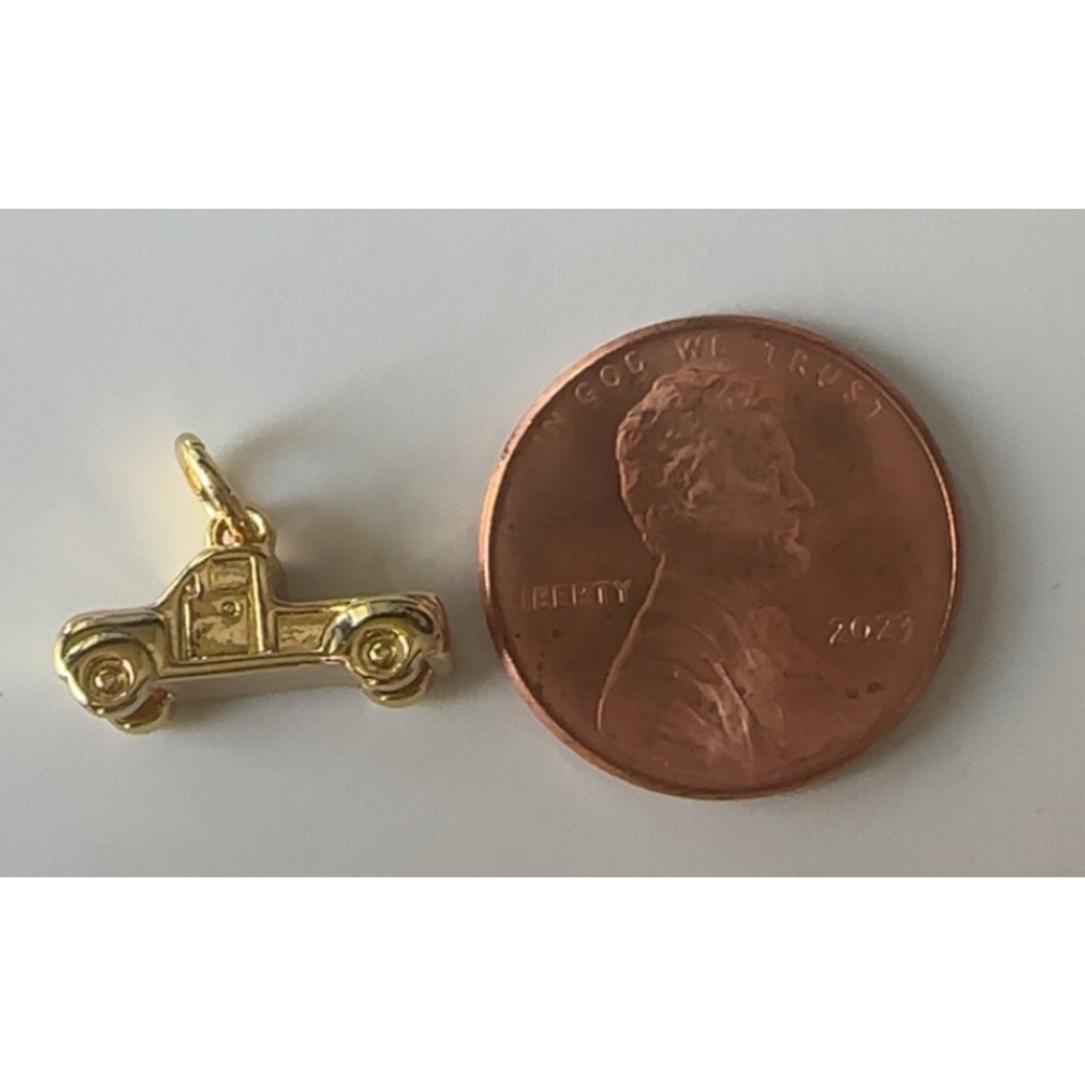 Gold truck charm next to a penny on a white background