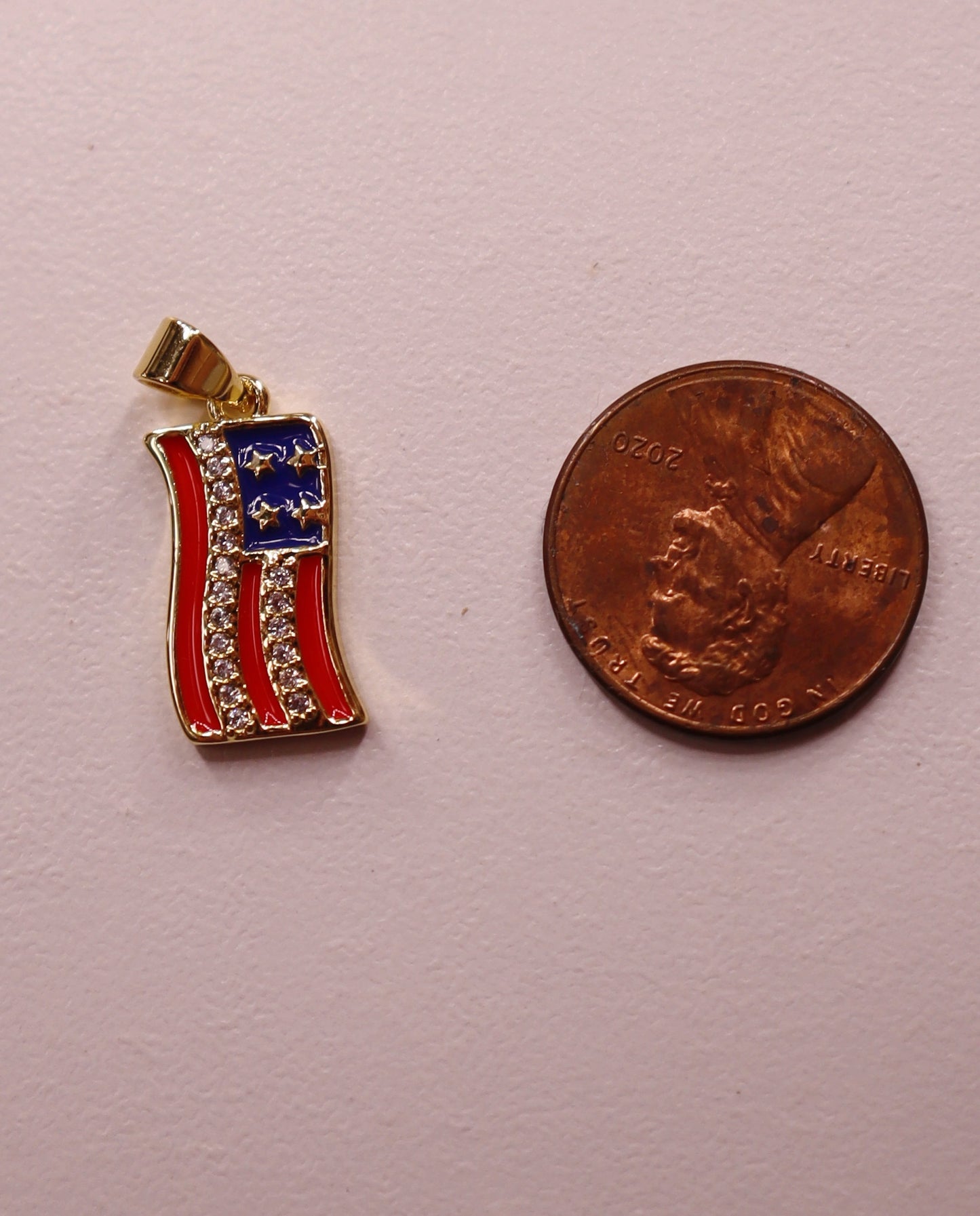 American flag pendant next to a penny on a pink background