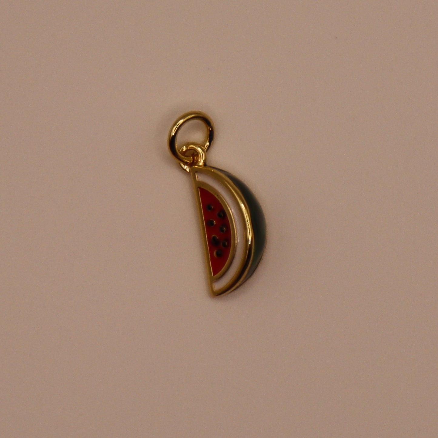 Gold charm shaped like a watermelon slice on a beige background
