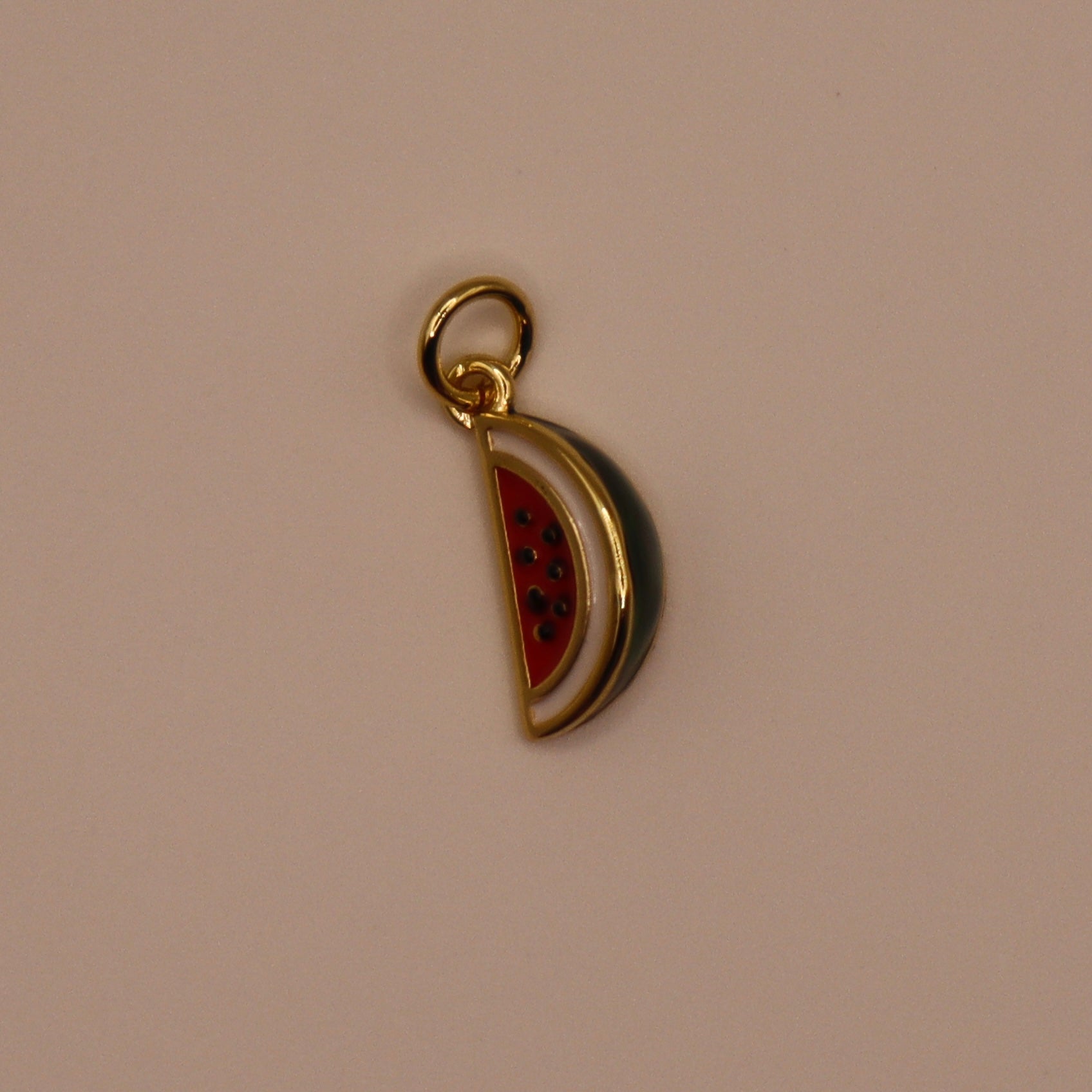 Gold charm shaped like a watermelon slice on a beige background