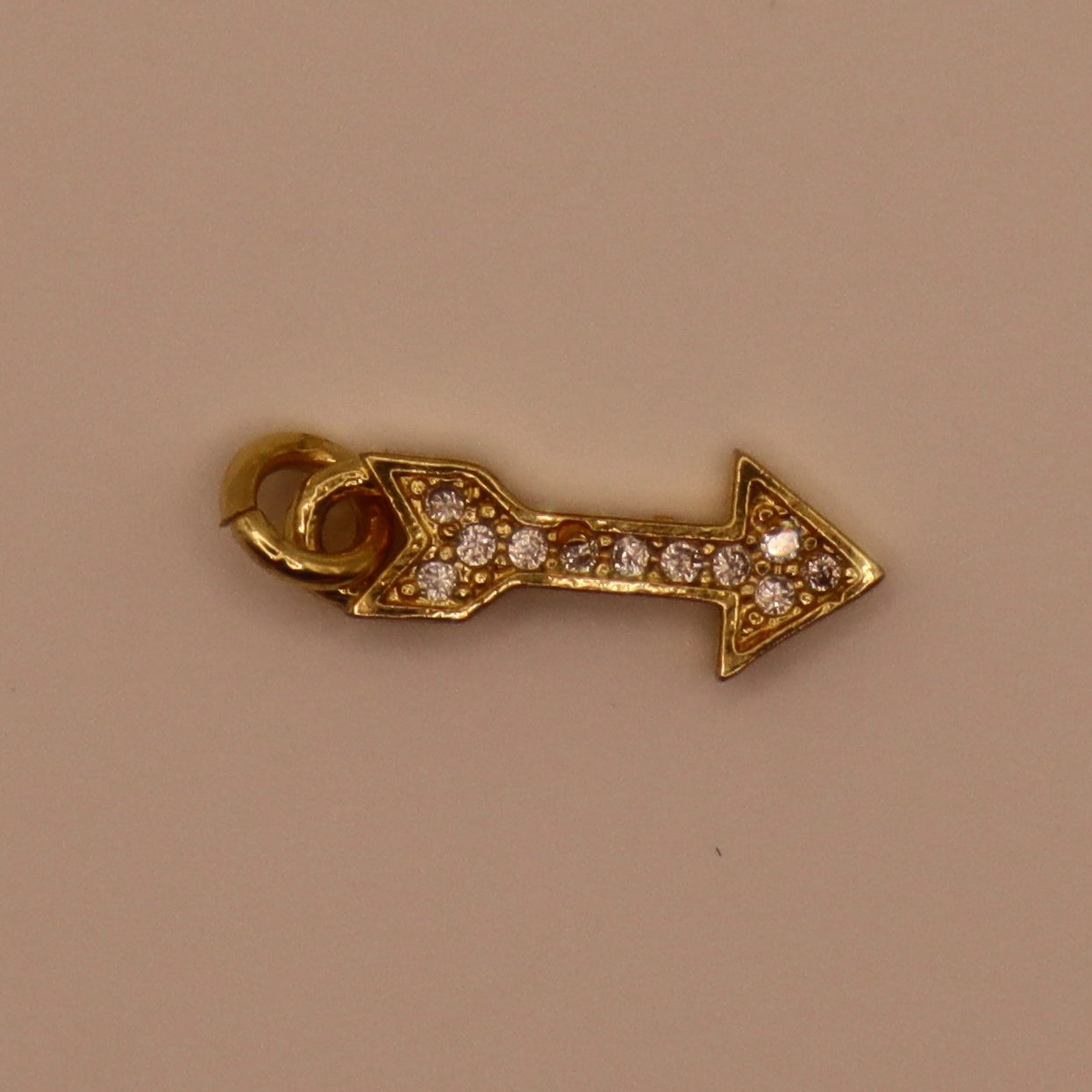 Gold arrow shaped pendant with diamond-like stones on a beige background