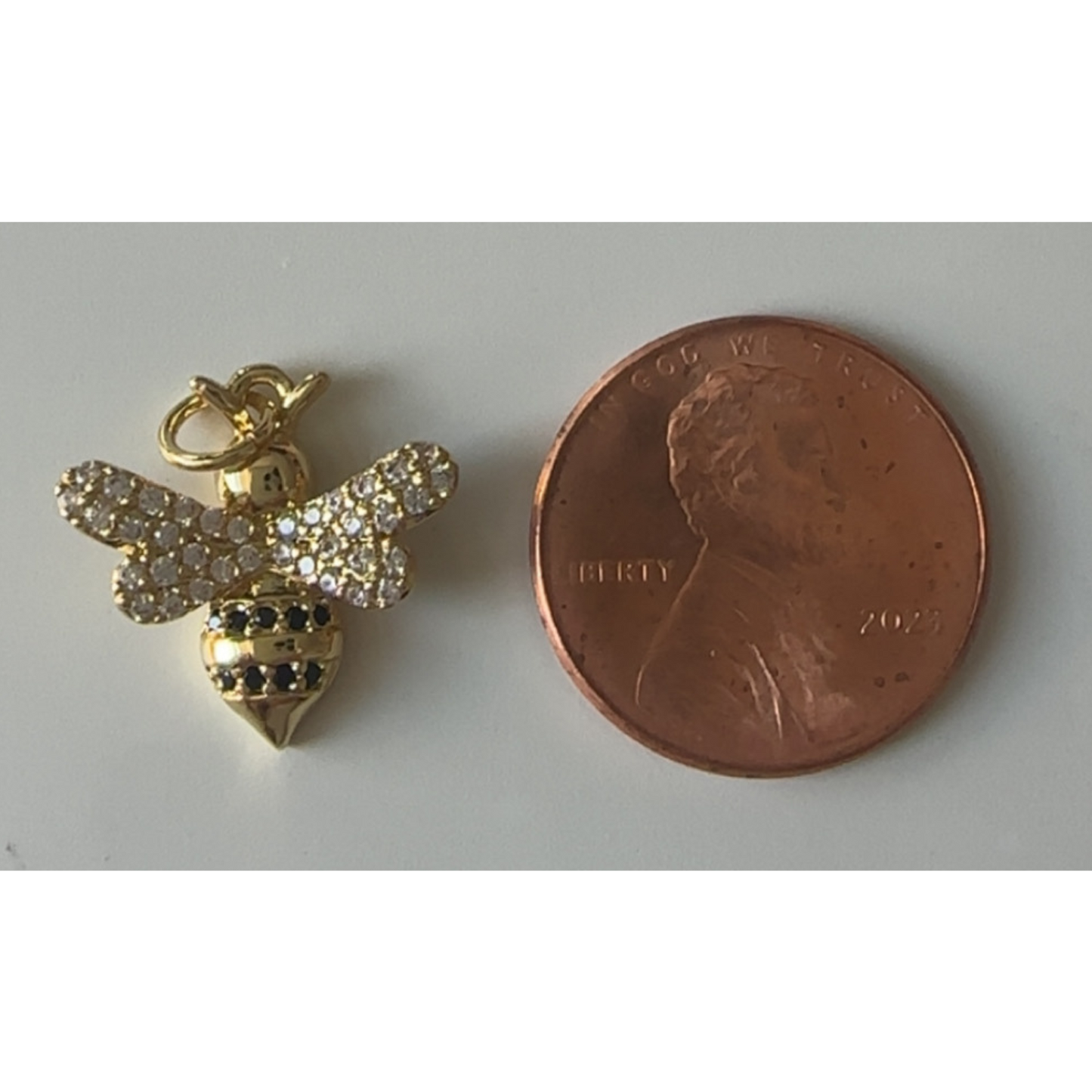 Gold bee charm next to a penny on a white background
