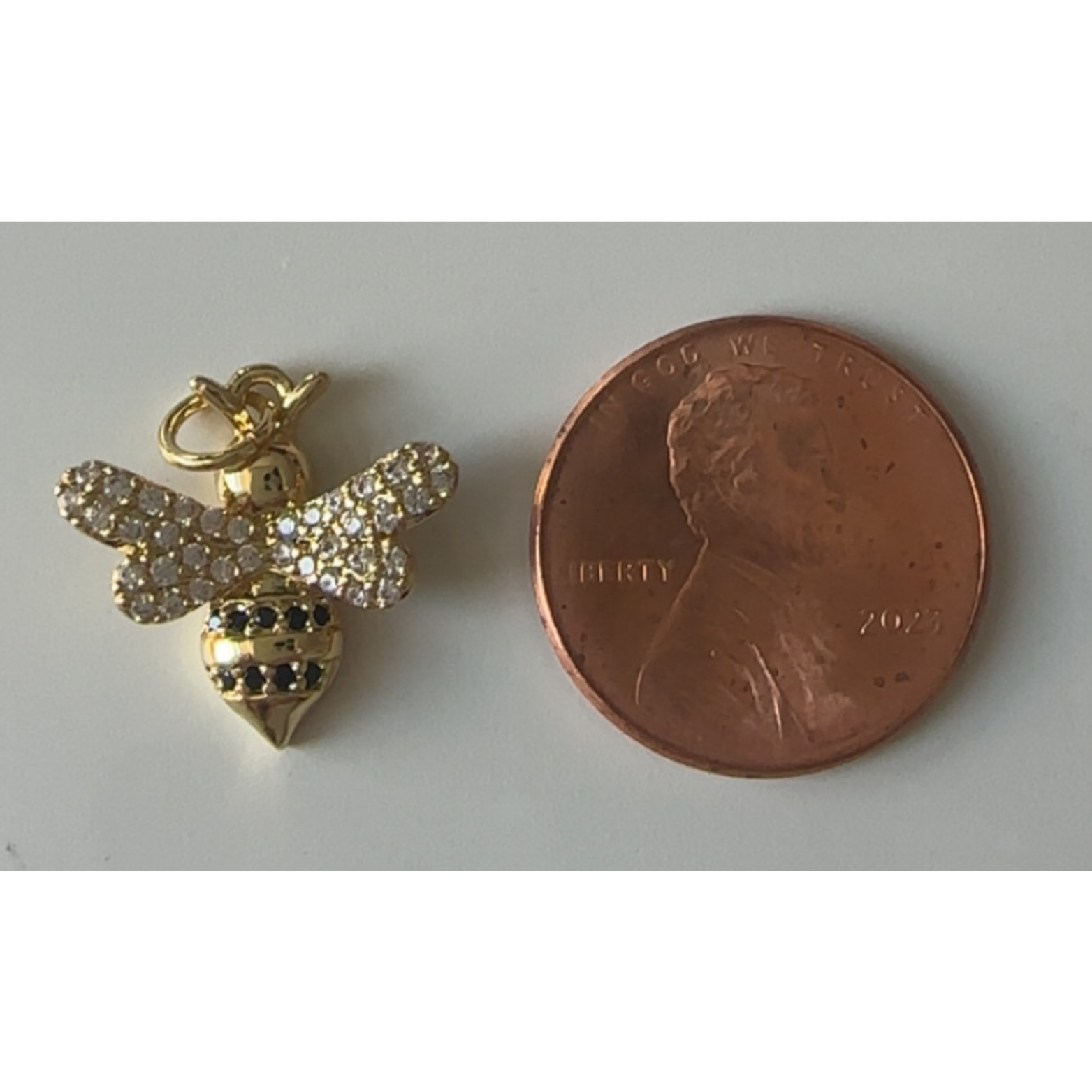 Gold bee charm next to a penny on a white background