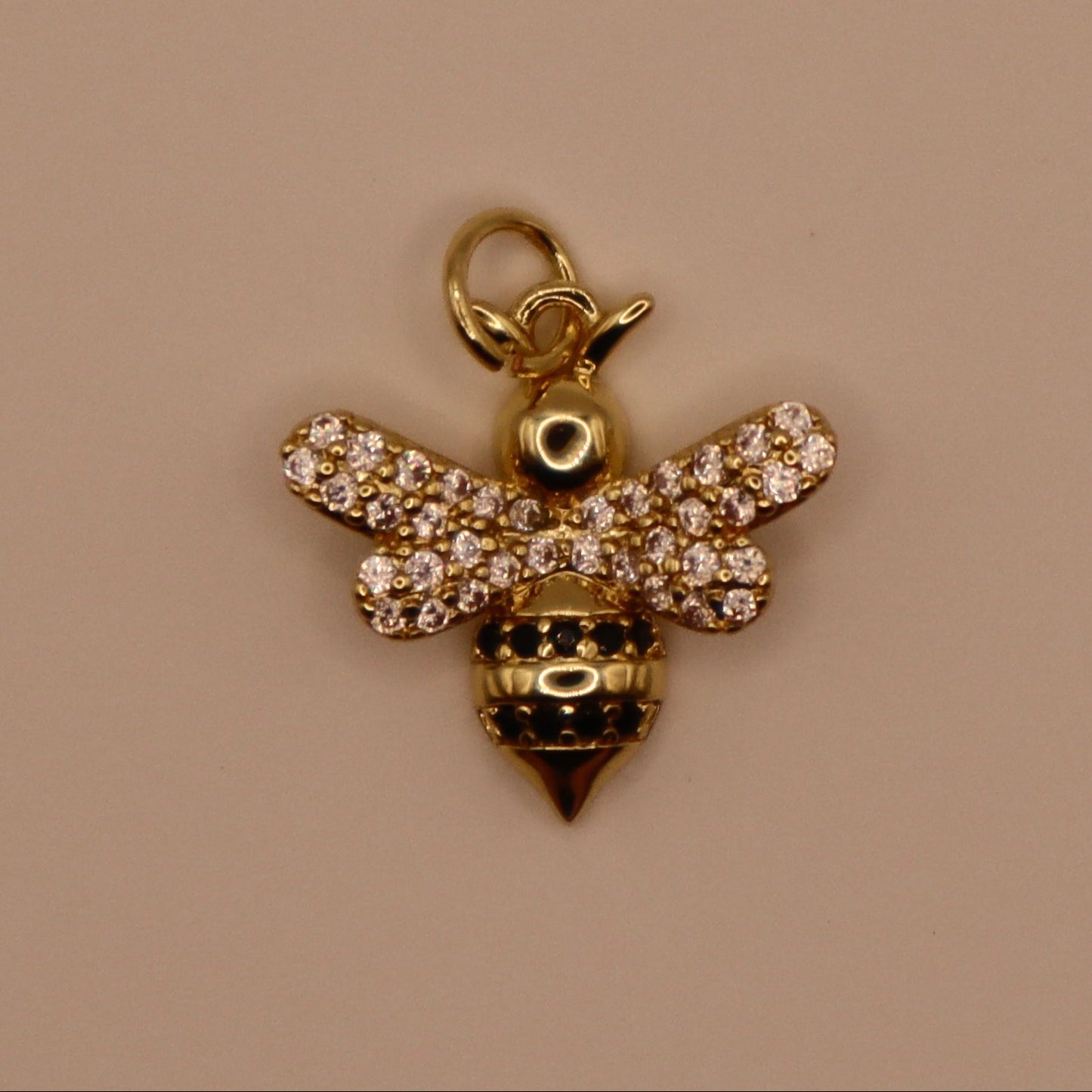 Gold bee charm with rhinestones on a beige background
