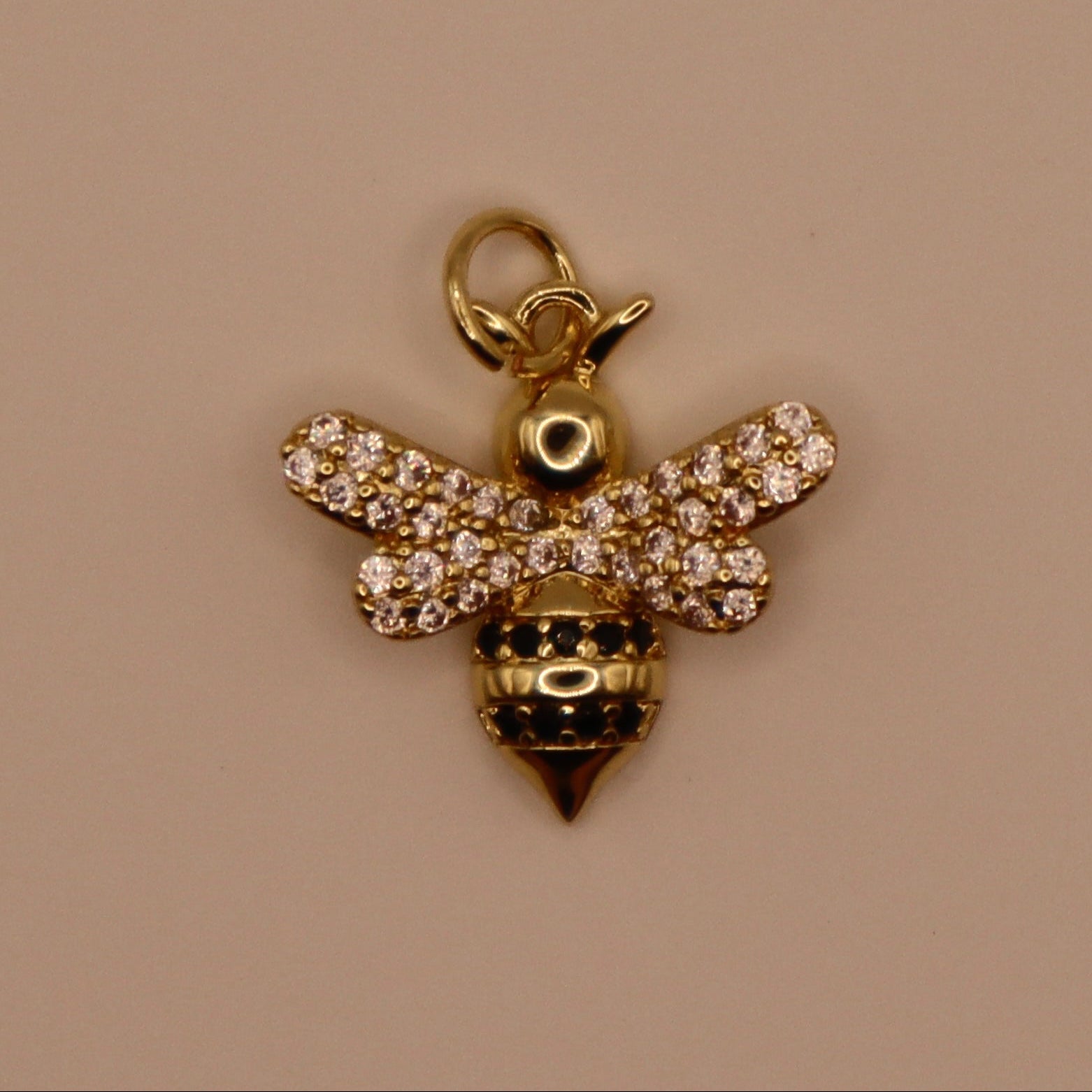 Gold bee charm with rhinestones on a beige background
