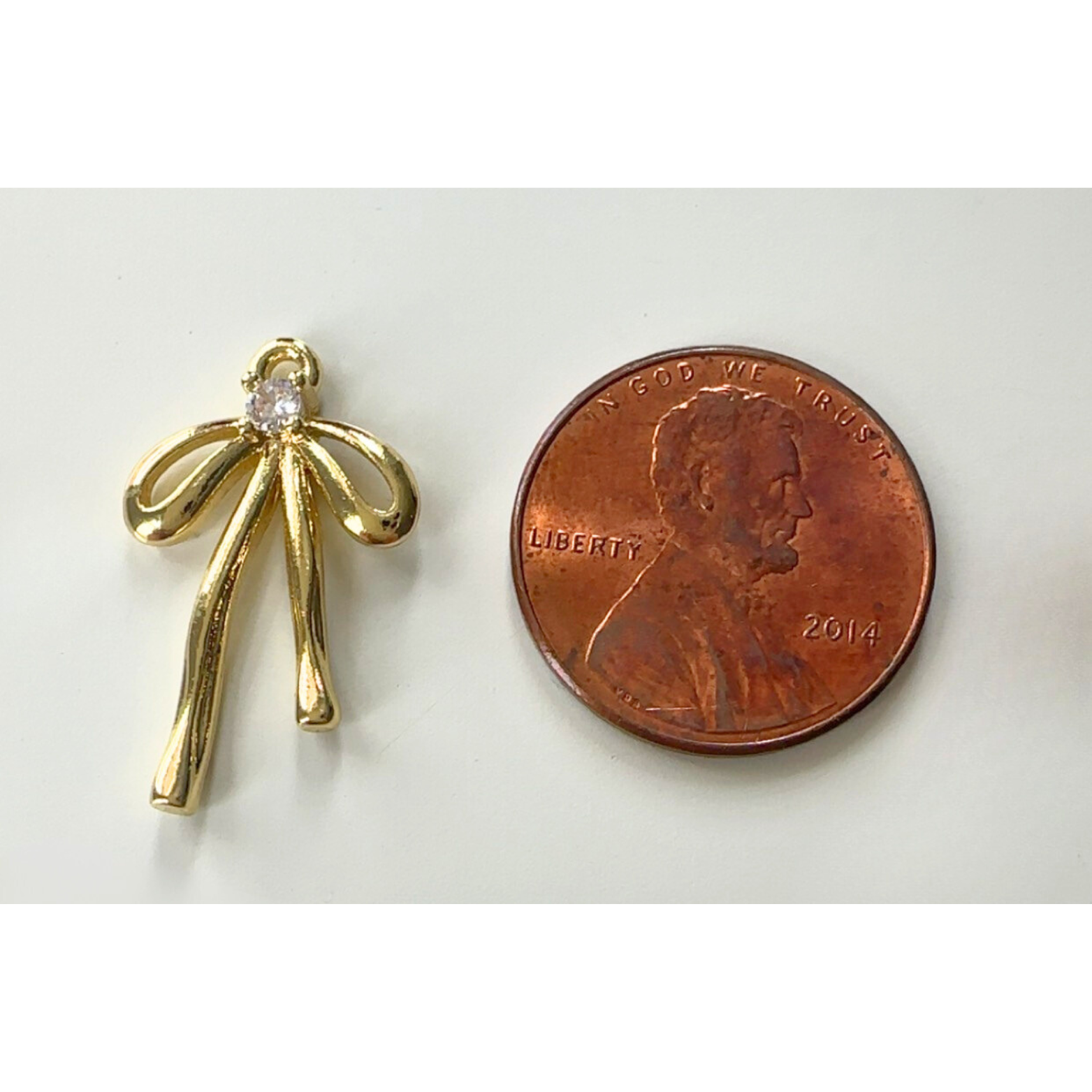 Gold bow-shaped pendant next to a penny on a white background