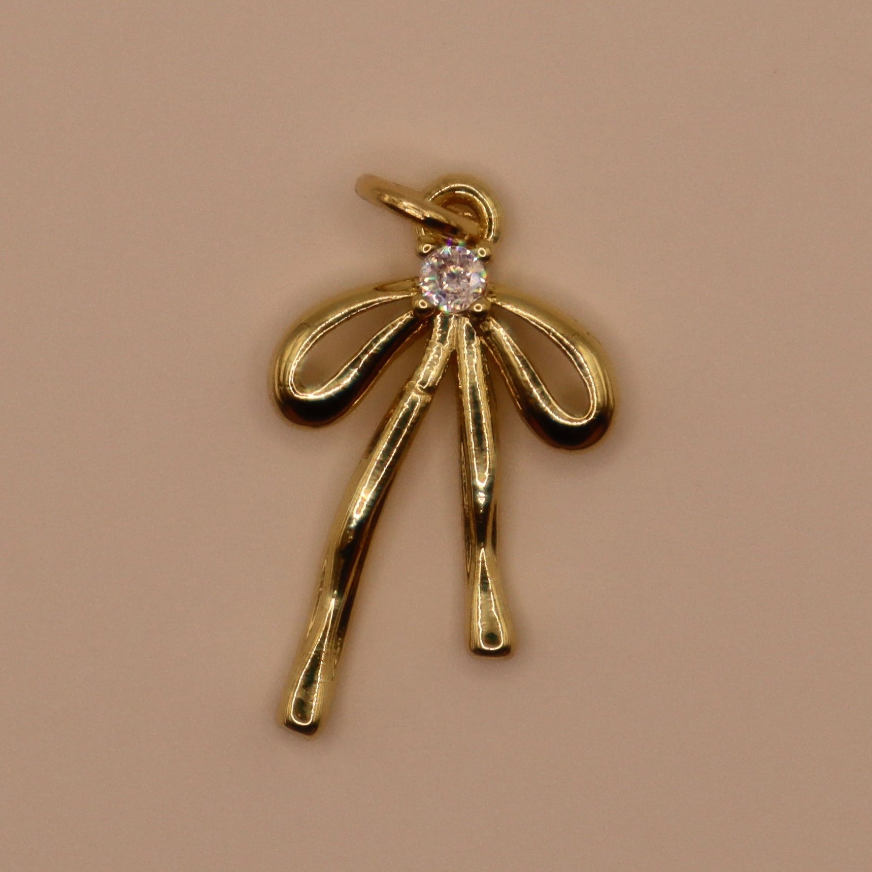 Gold bow-shaped pendant with a diamond on a beige background