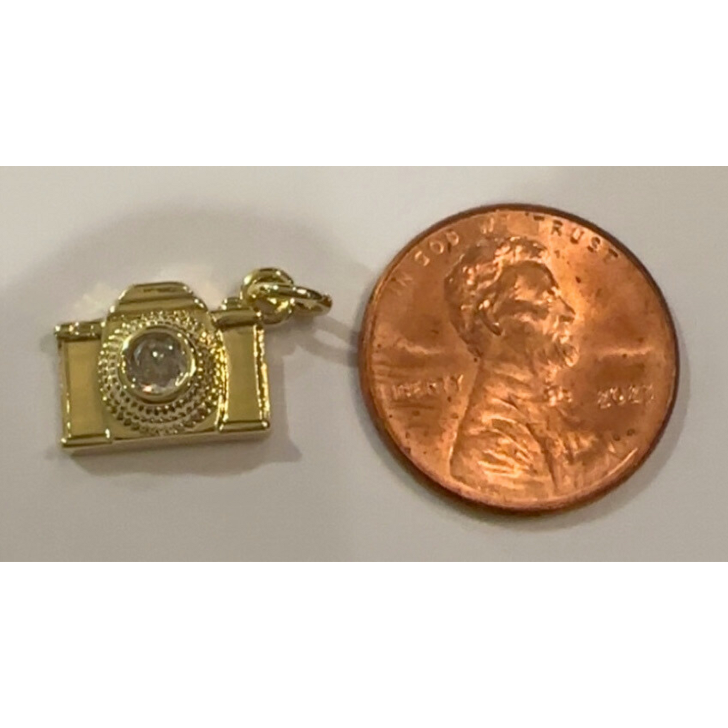 Gold camera charm next to a penny on a white background