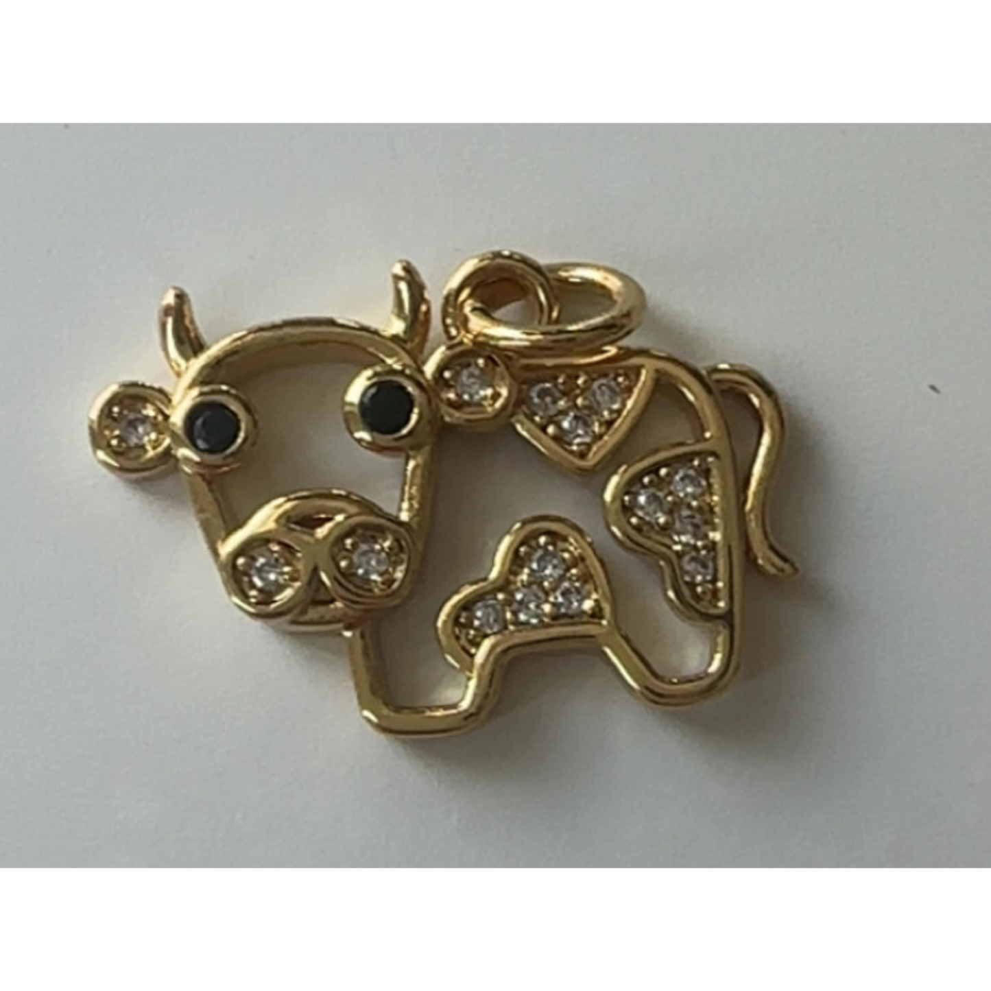 Gold cow pendant with black eyes and clear stones on a light gray background