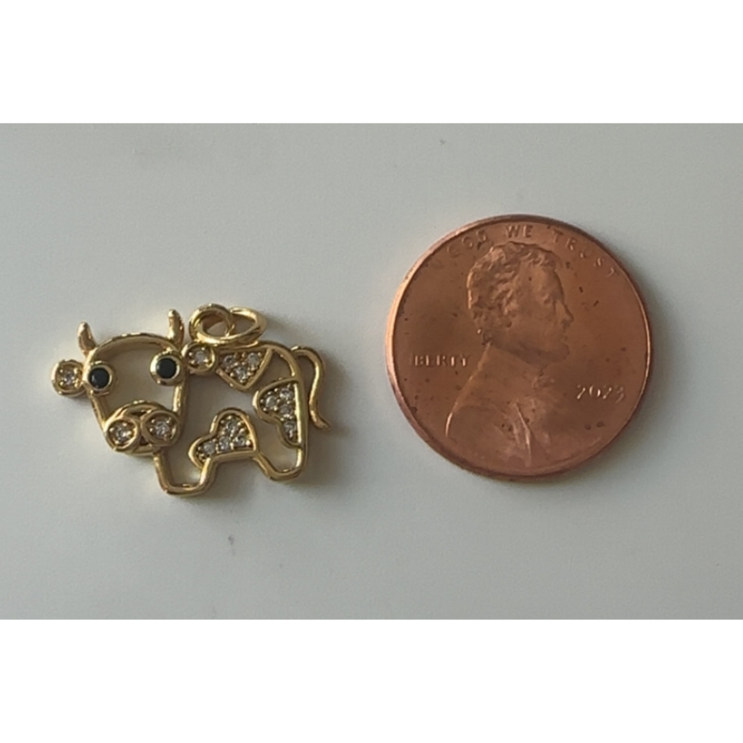 Gold cow pendant next to a penny on a gray background