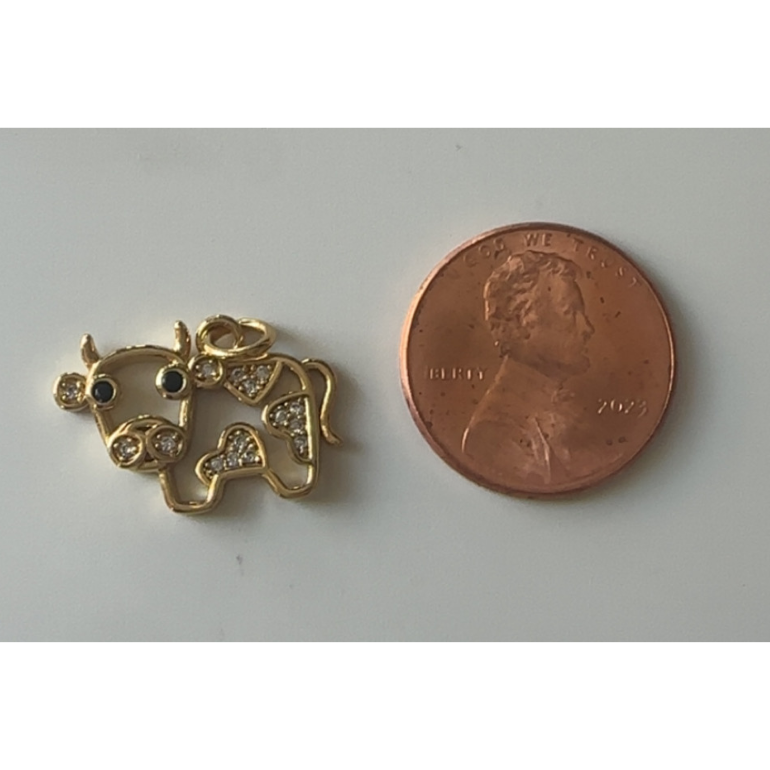 Gold cow pendant next to a penny on a gray background