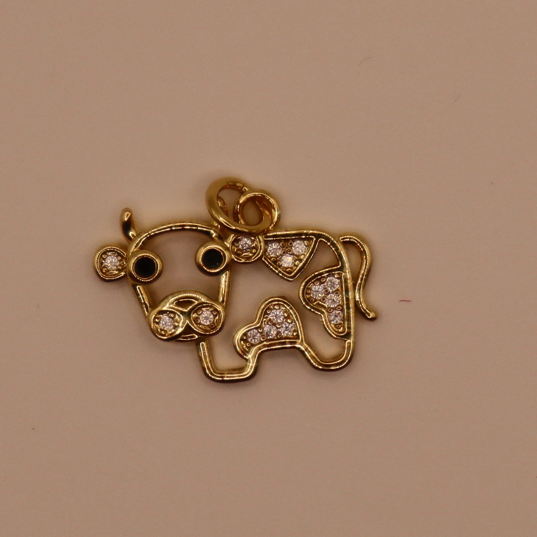 Gold cow-shaped pendant with rhinestones on a beige background