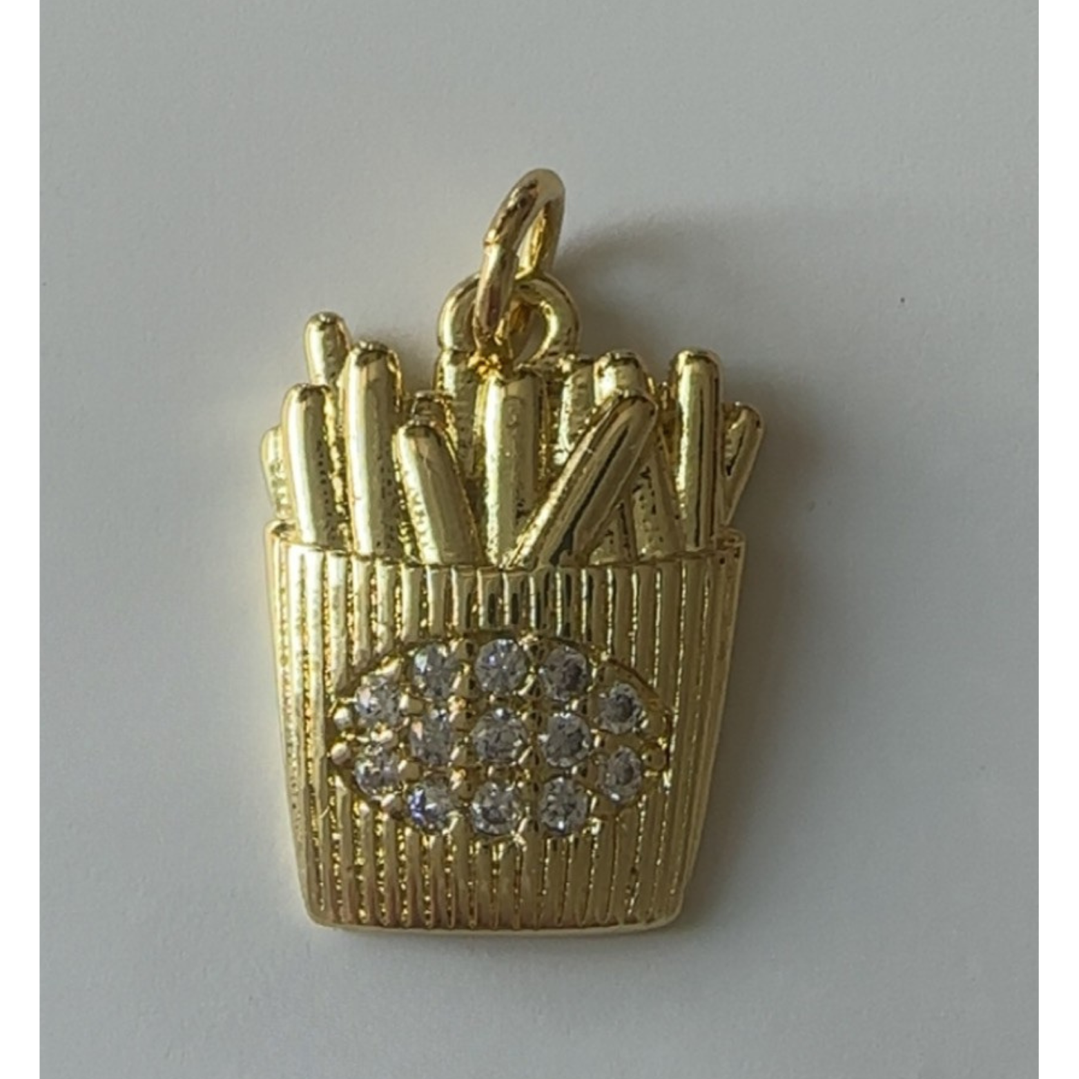 Gold pendant shaped like a basket of fries with rhinestones on a gray background