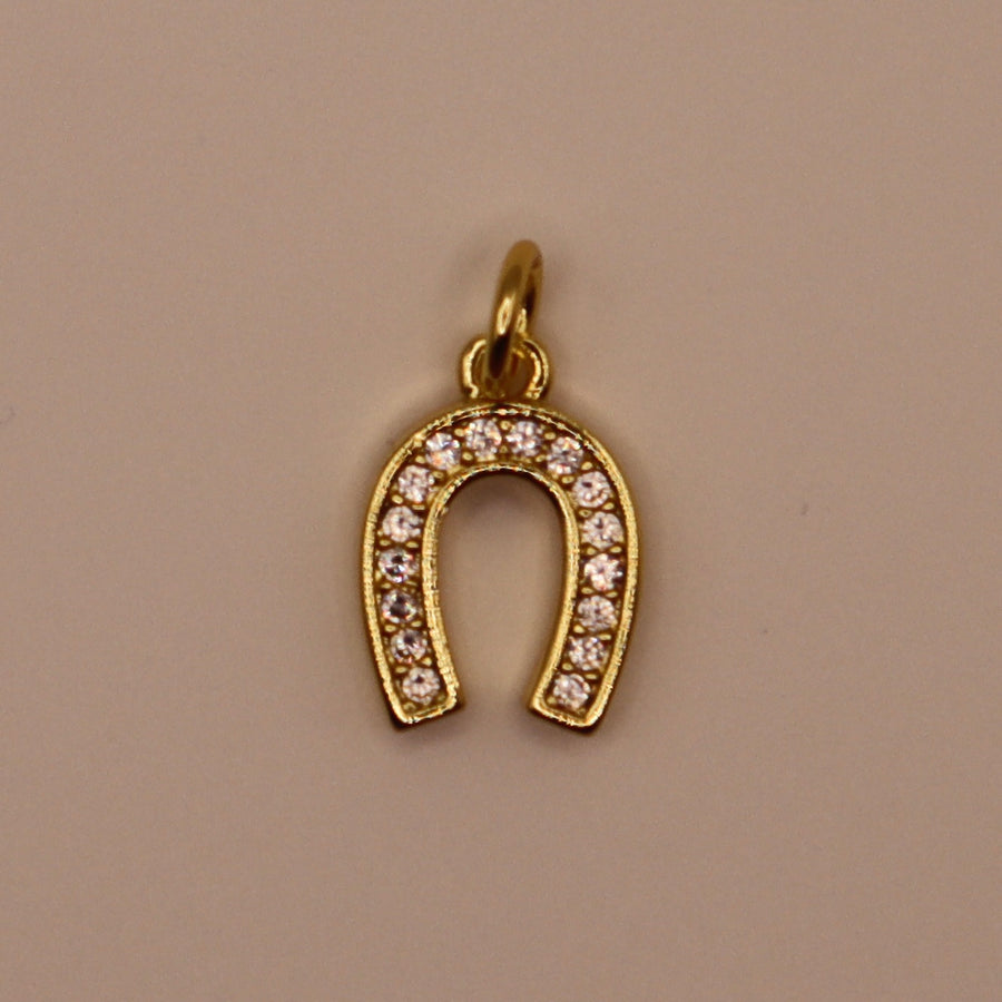 Gold horseshoe-shaped pendant with embedded stones on a beige background