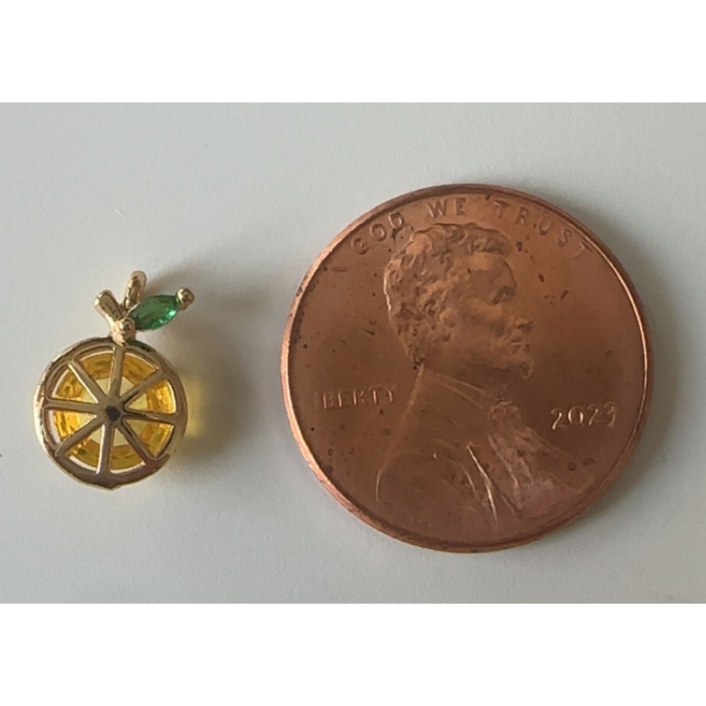 Small gold lemon charm next to a penny on a white background