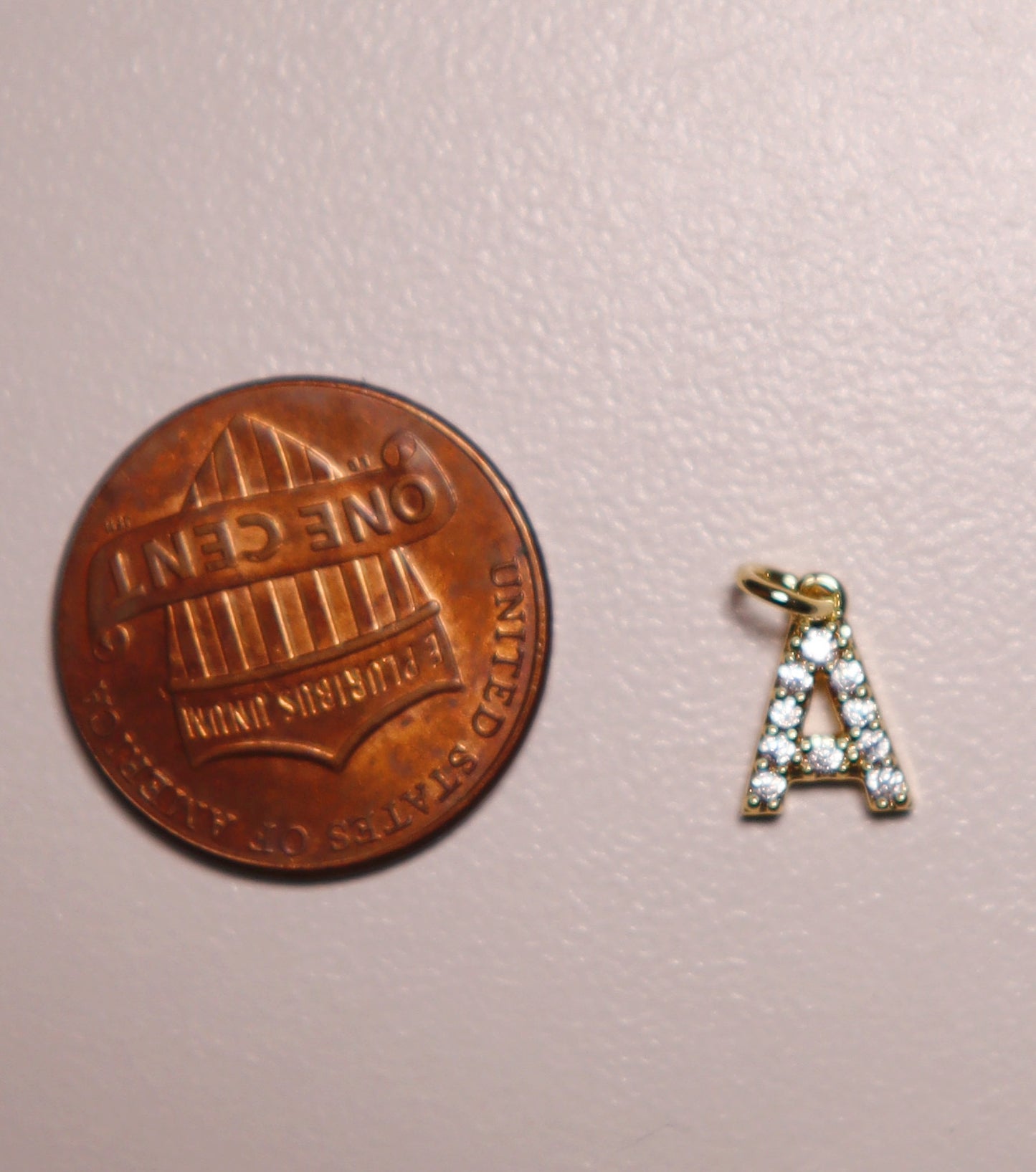 Small gold letter 'A' charm next to a penny on a pink background