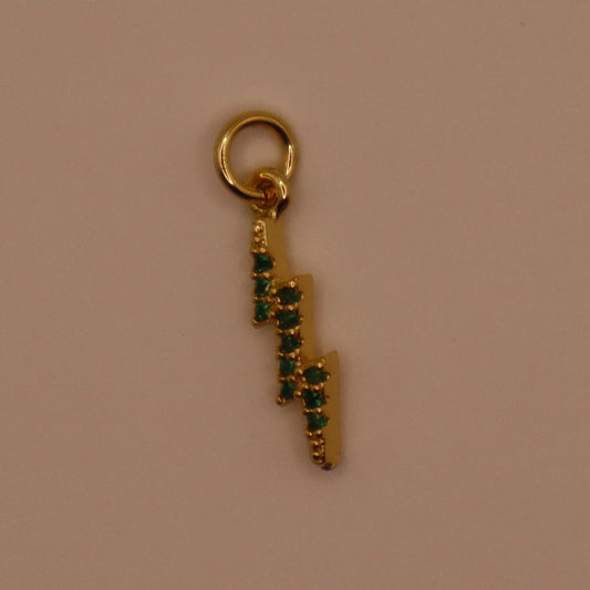 Gold lightning bolt charm with green stones on a beige background