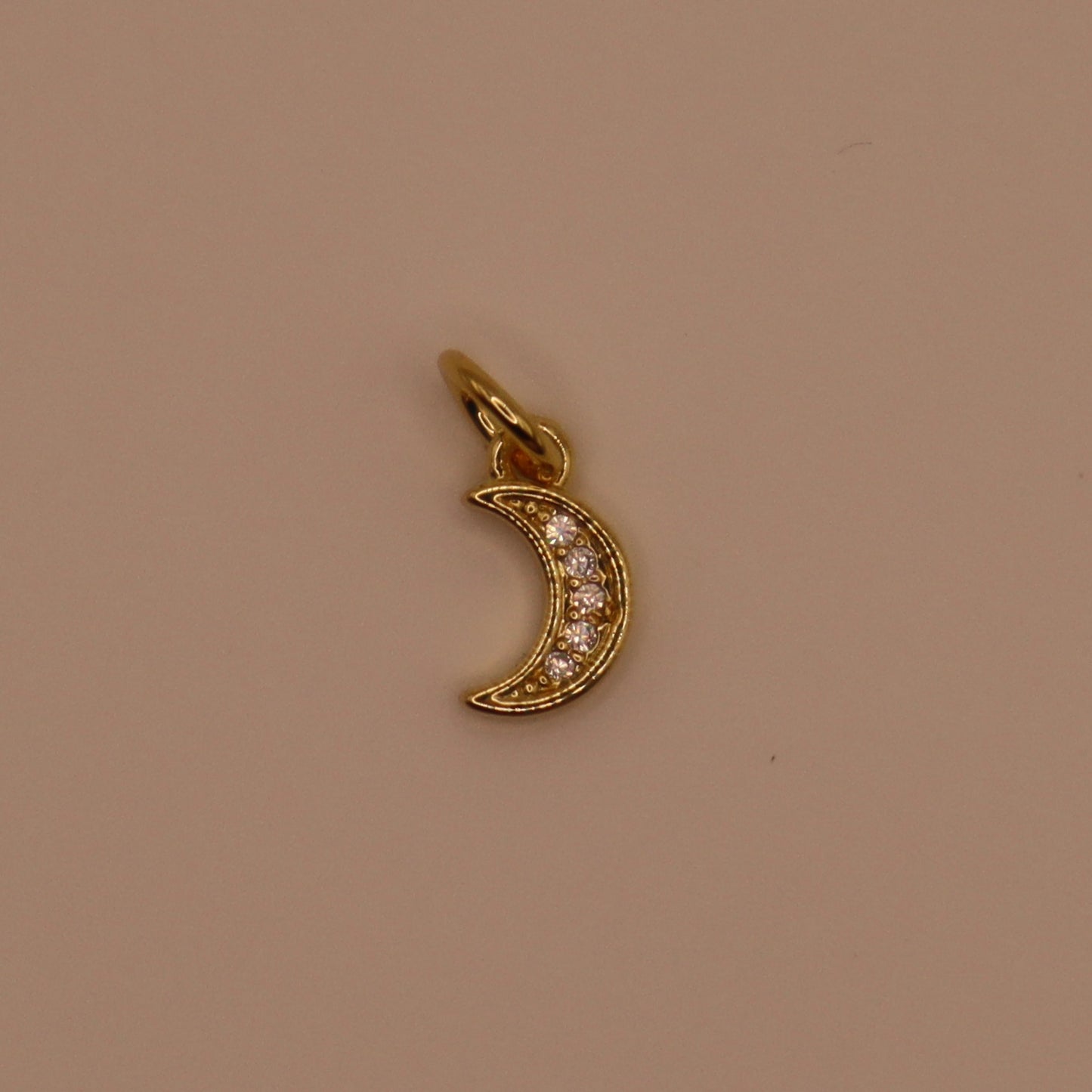 Gold crescent moon charm with embedded stones on a beige background