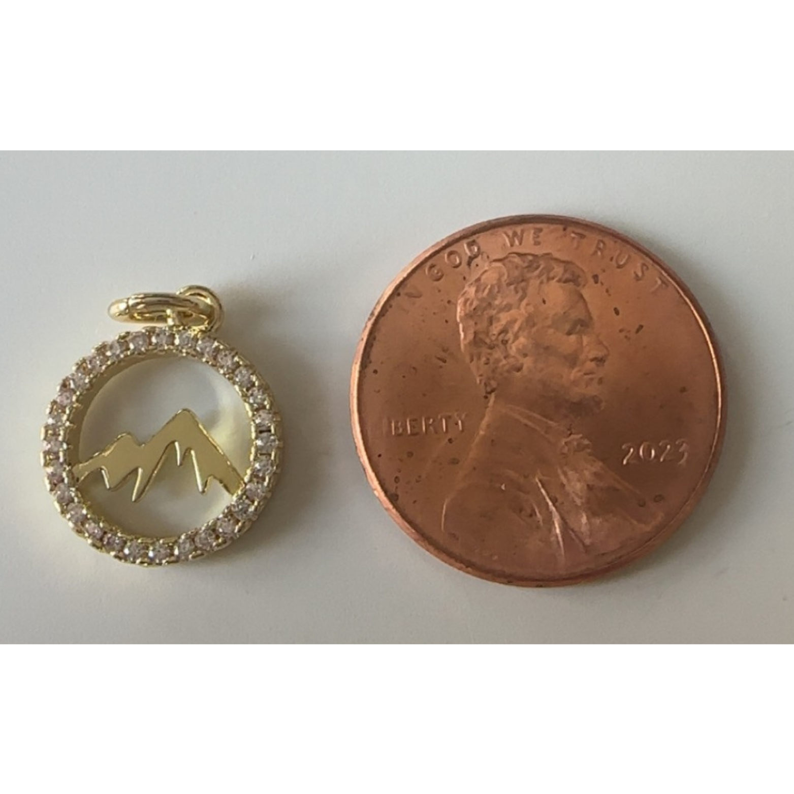 Gold pendant with mountain design next to a penny on a white background