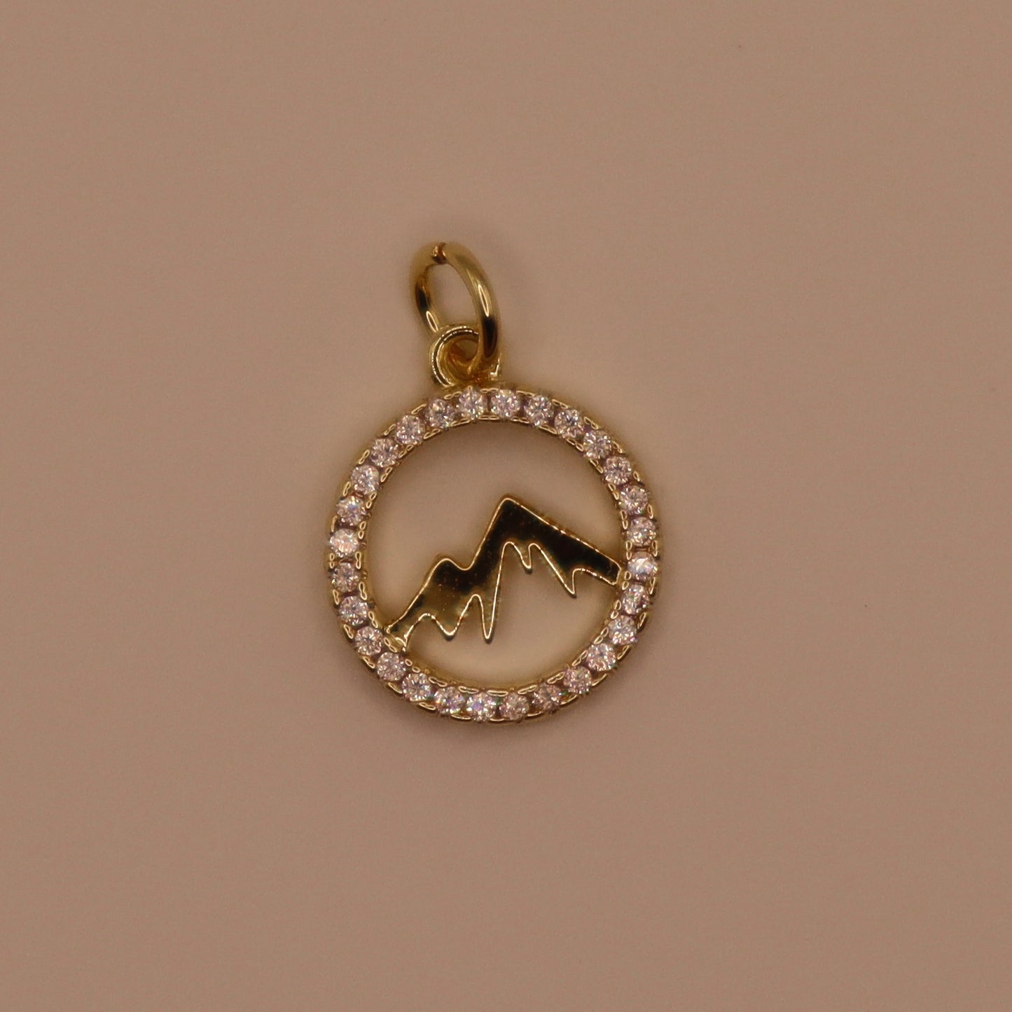 Gold charm with mountain design and diamond accents on a brown background